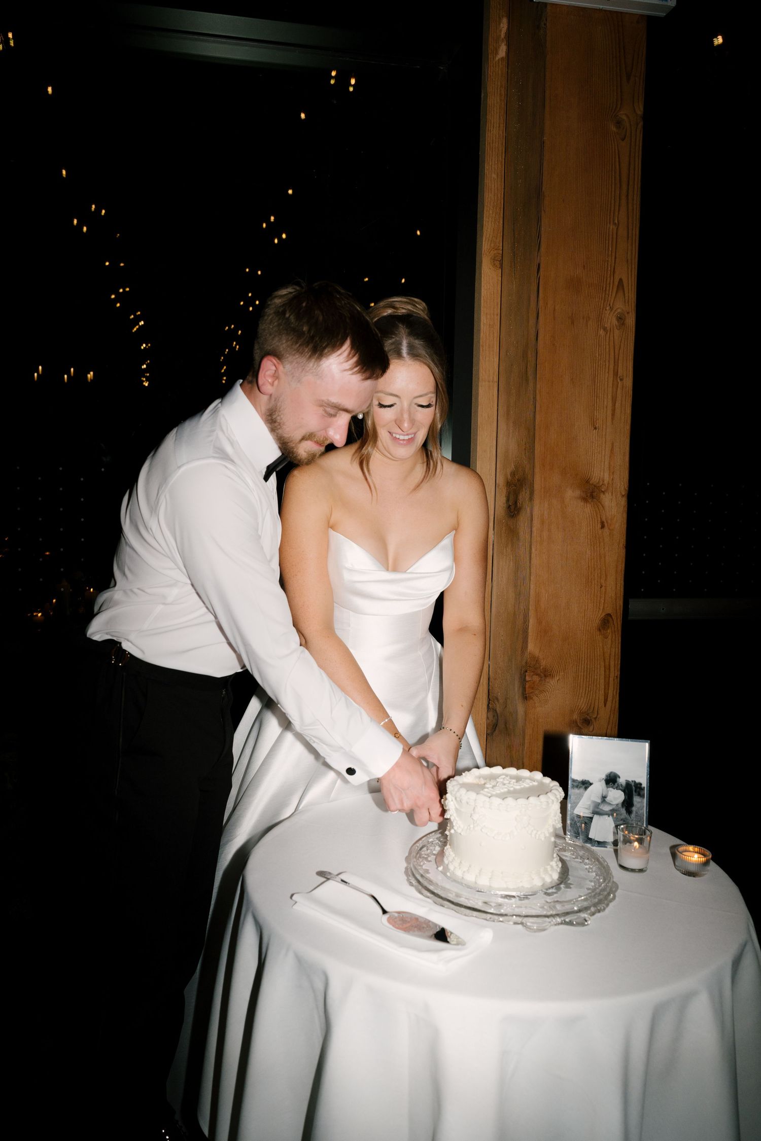 Bride and groom cutting their white wedding cake together at a romantic evening reception at Pillar and Post.