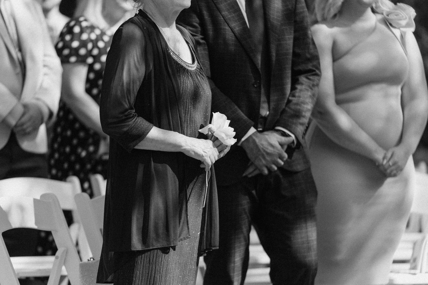 Black and white photo of elegantly dressed wedding guests standing during an outdoor ceremony at Roseville Estates wedding venue.