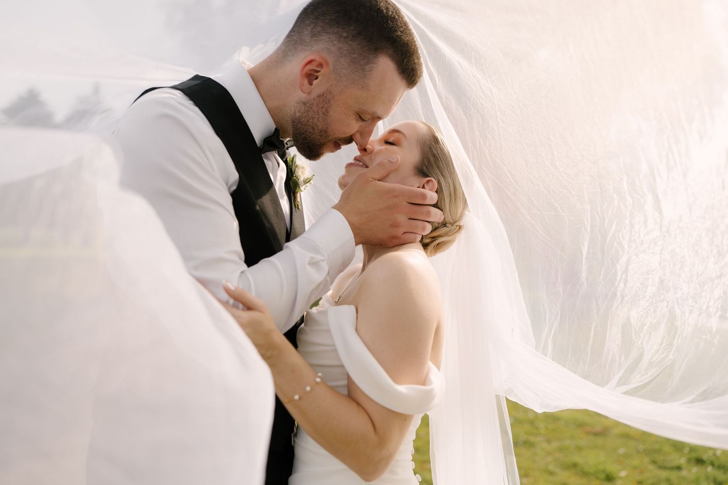 Bride and groom share an intimate moment under a flowing white veil on their wedding day.