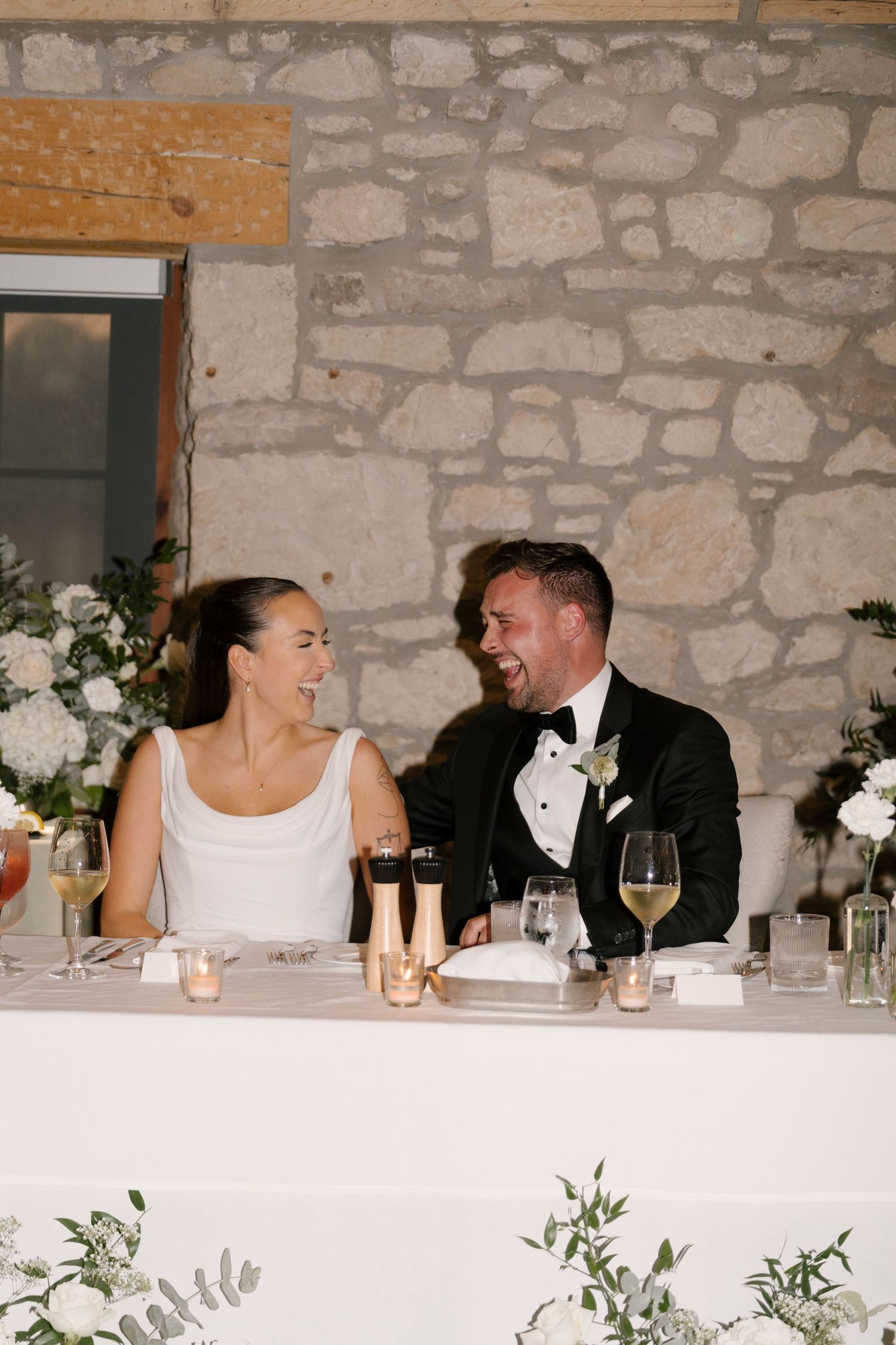 Bride and groom sharing a laugh together at the sweetheart table during wedding reception at Cambridge Mill.