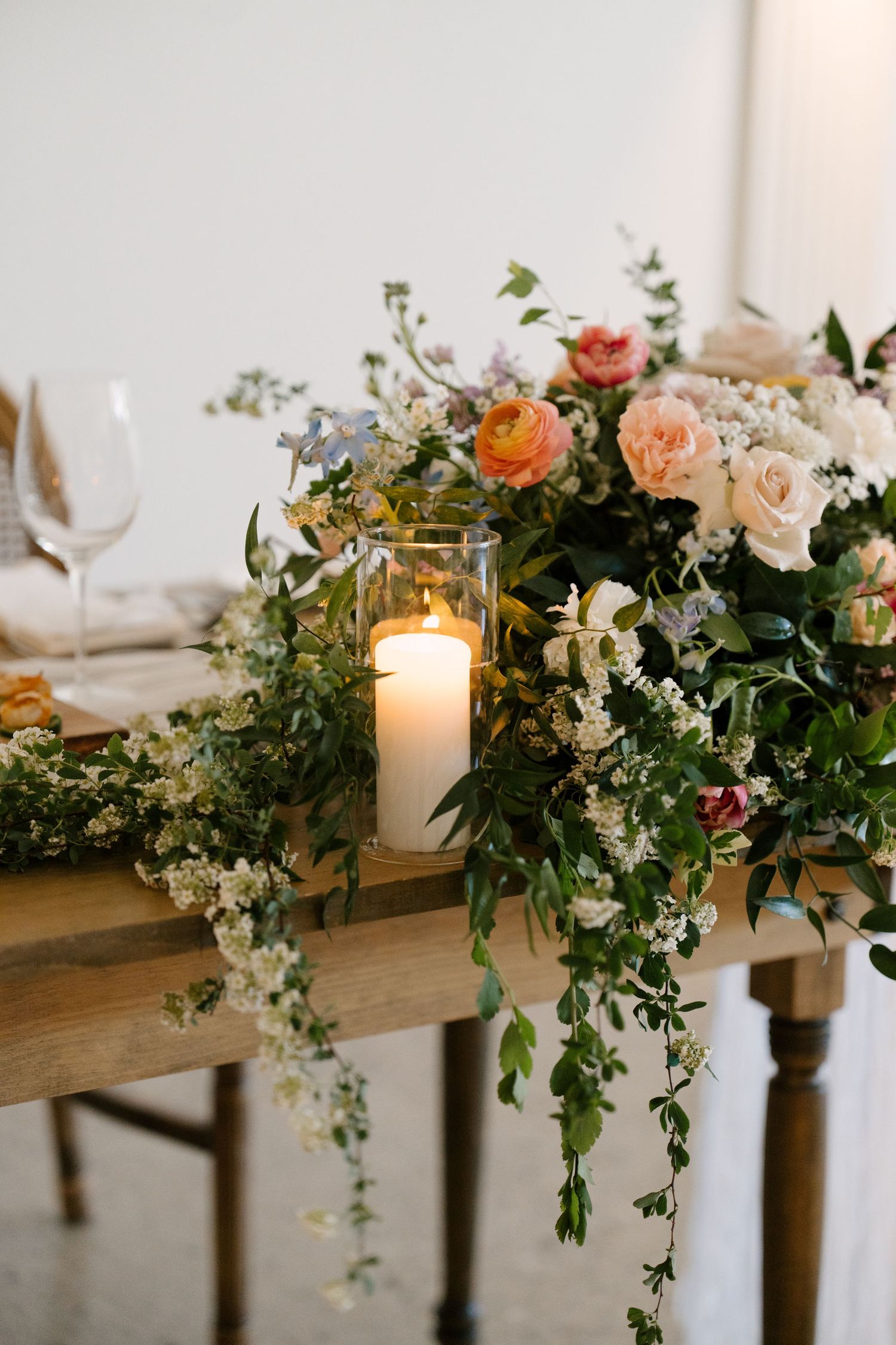 Lush floral centrepiece with pink roses and candle cascading over a rustic wooden table at Roseville Estates wedding venue.