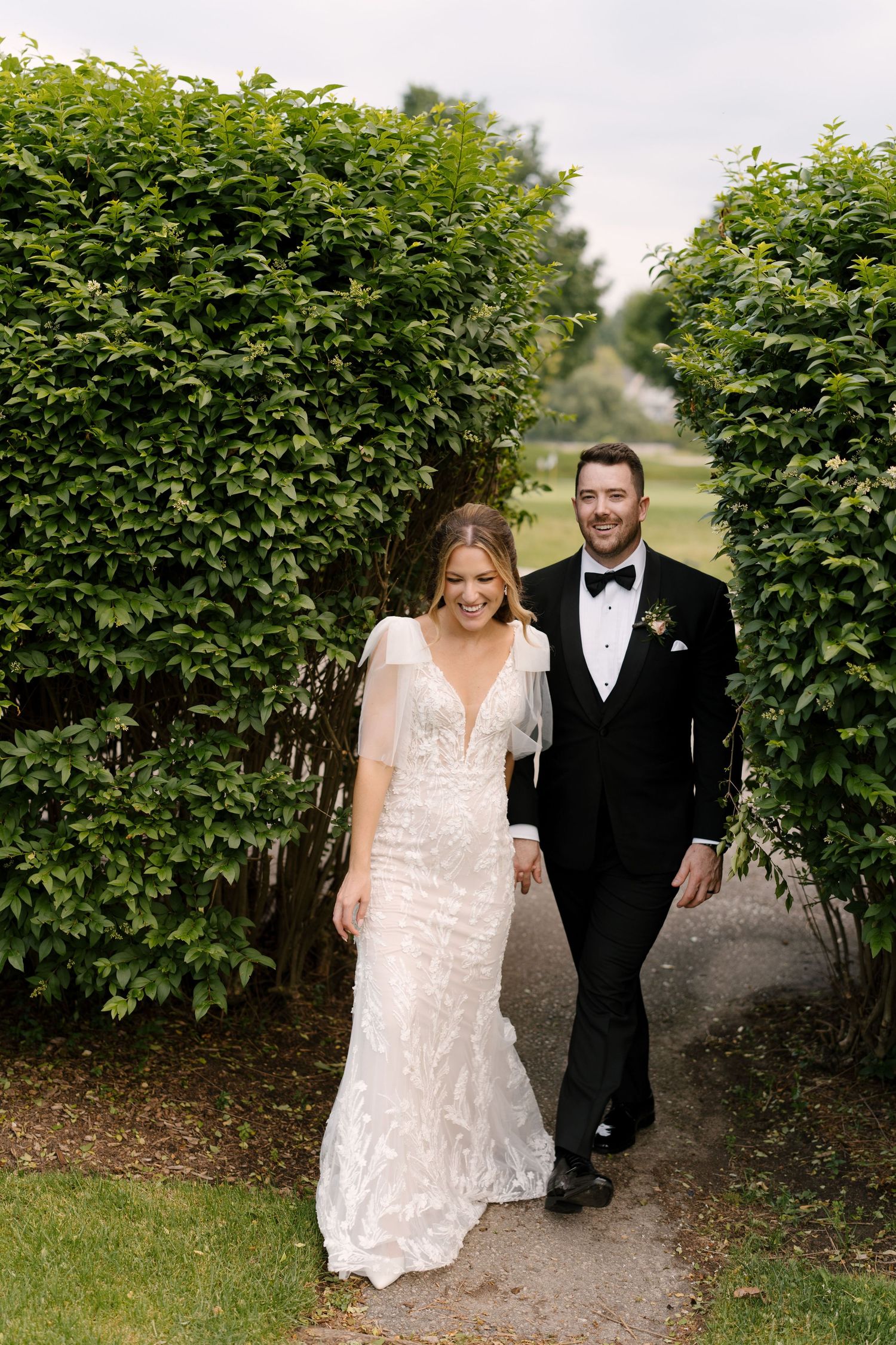 Bride and groom walking through a lush green hedge archway laughing on their wedding day at St Marys Golf Club.