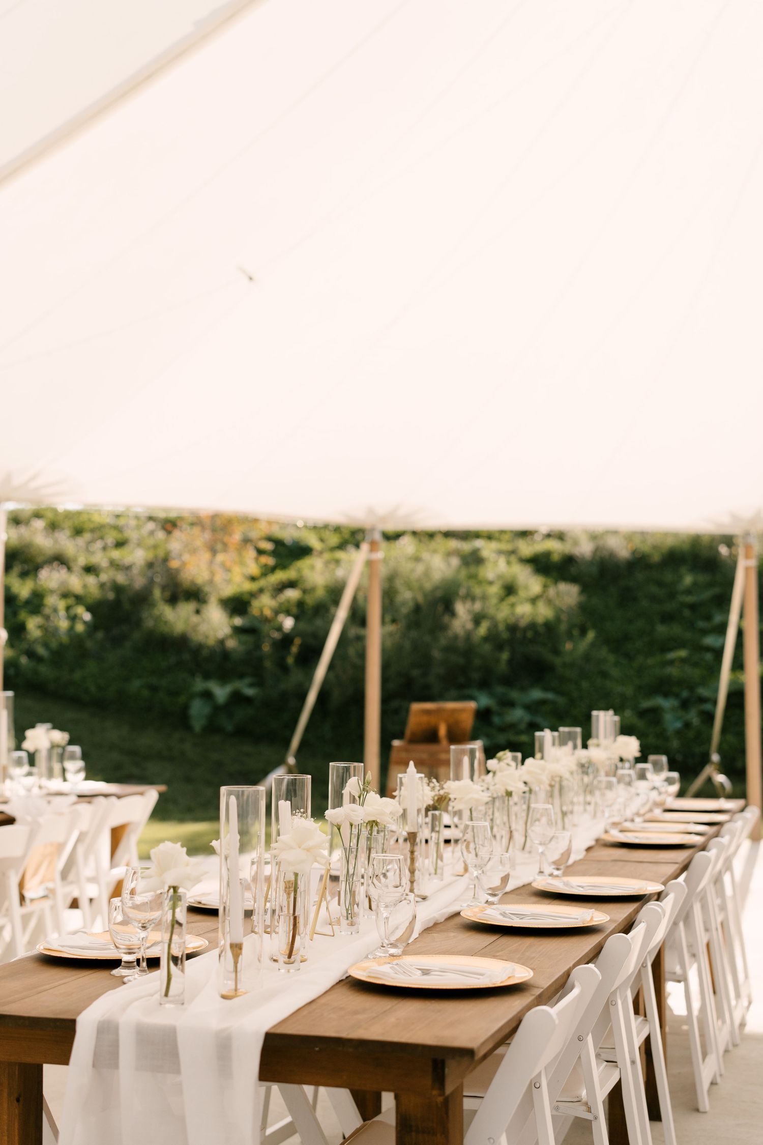 Elegant outdoor wedding reception table set under a white tent with white linens, candles, and floral centrepieces at Wakefield Estates.