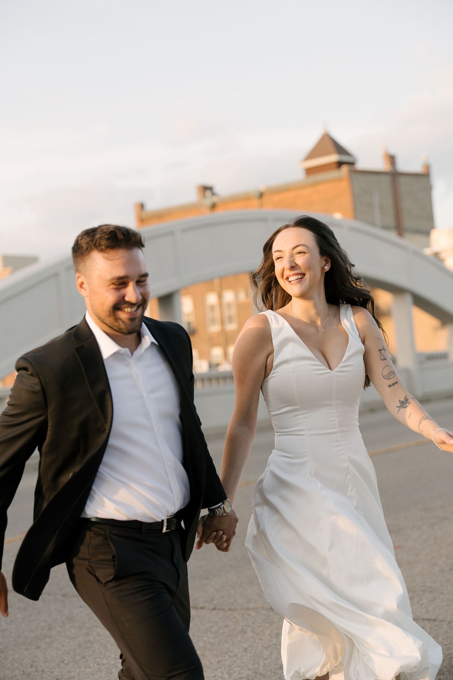 Joyful couple running and laughing together on a bridge during sunset engagement session.