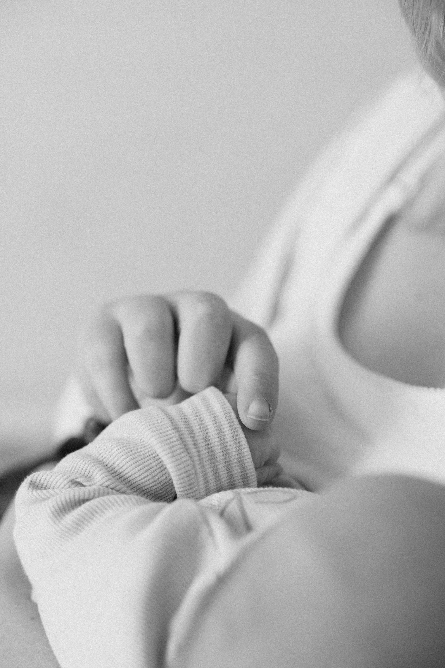 Close-up black and white photo of a newborn baby's tiny hand resting on an adult's chest.