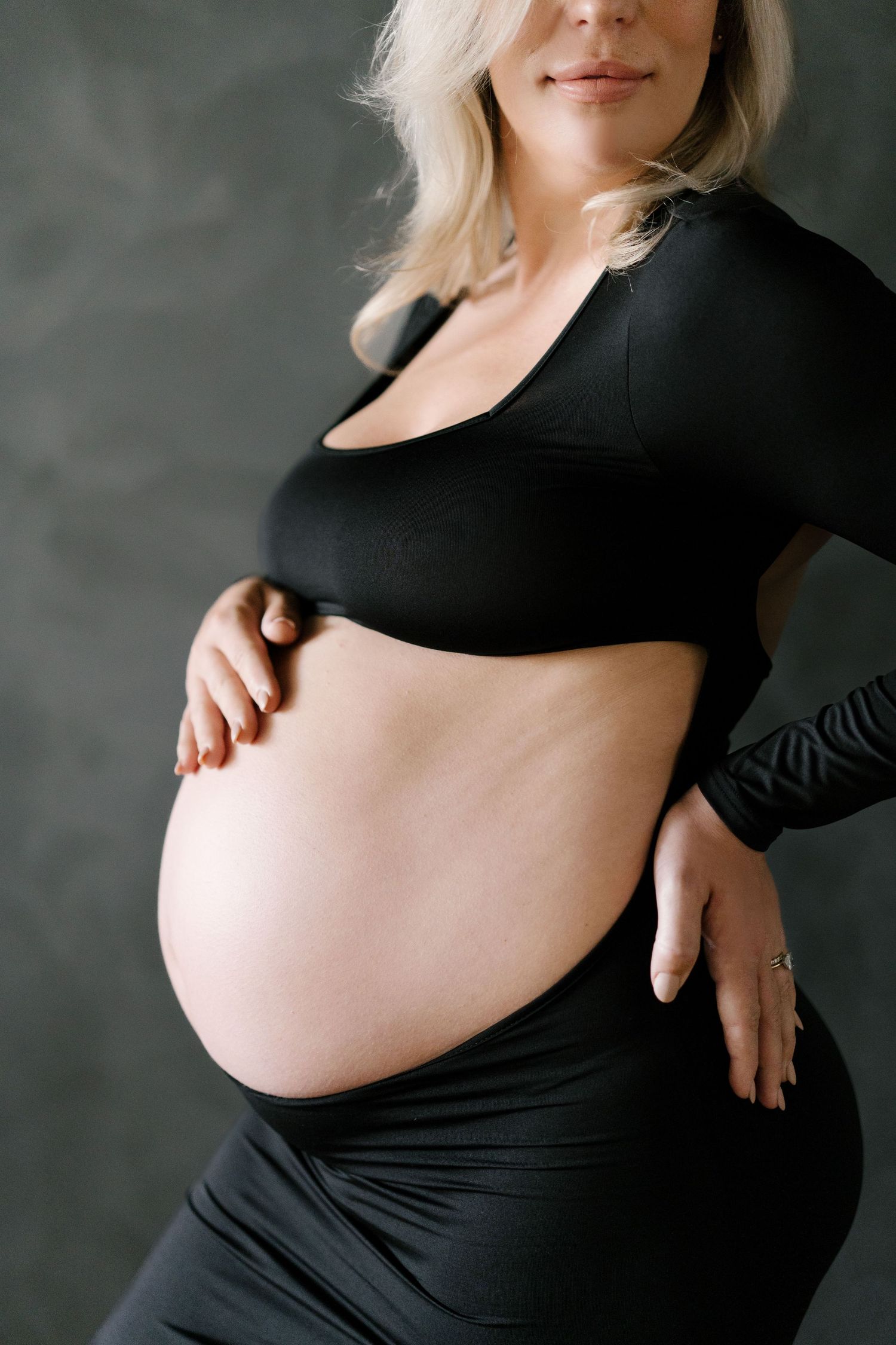 Close-up of pregnant woman in black crop top gently holding baby bump with both hands.