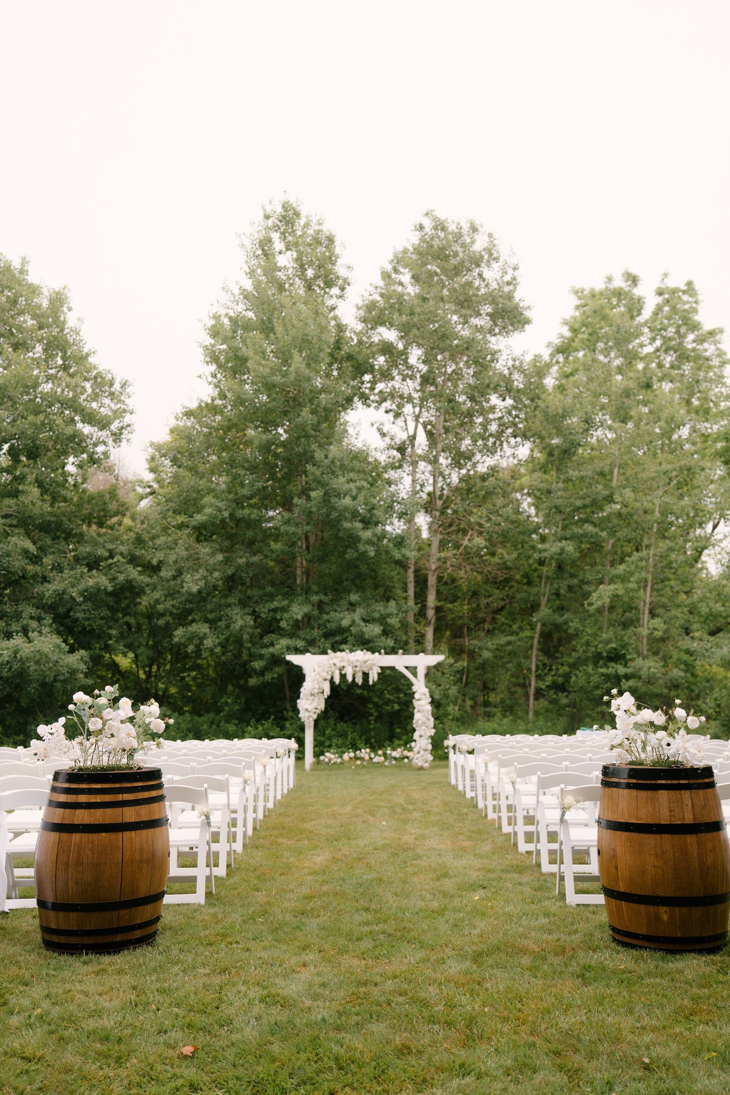 Elegant outdoor wedding ceremony setup with white chairs, floral arch, and rustic wine barrel decorations at Guelph Golf Club.