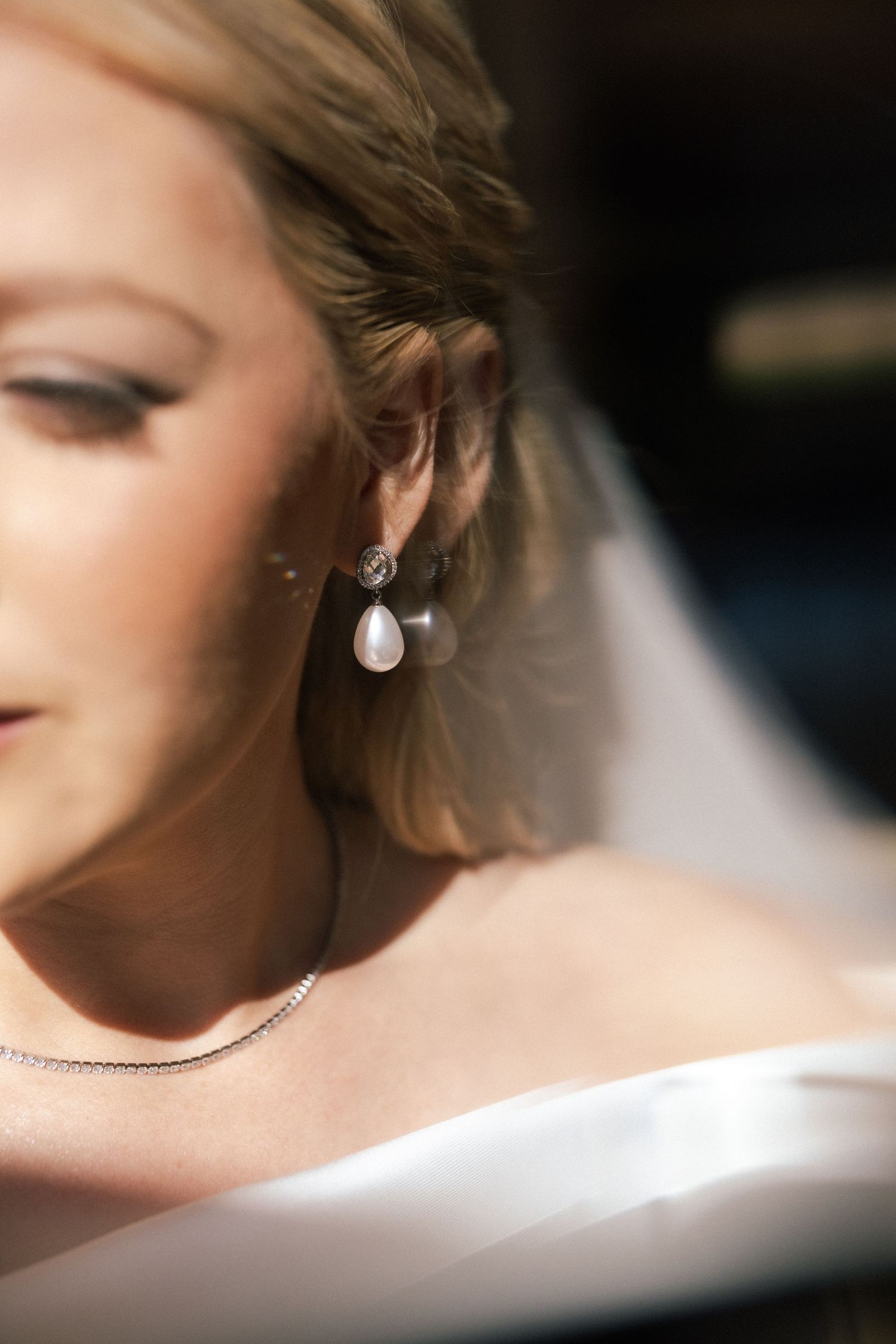 Close-up of pearl drop earring and bridal makeup in soft natural light.