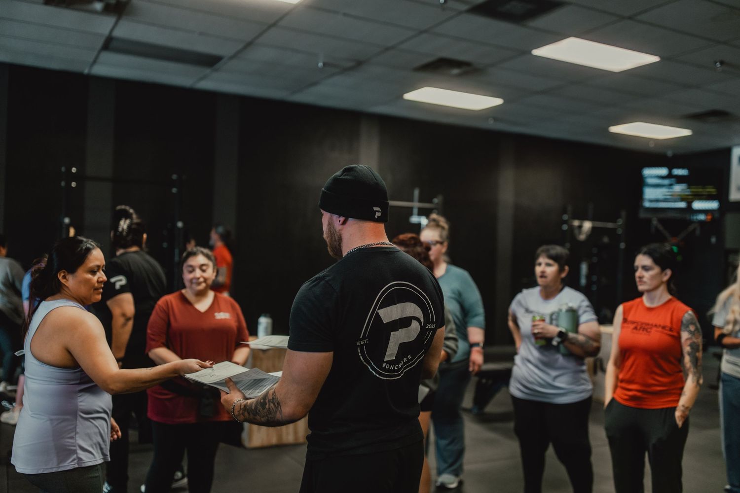 A group fitness class with participants gathered around an instructor in a dark indoor space.