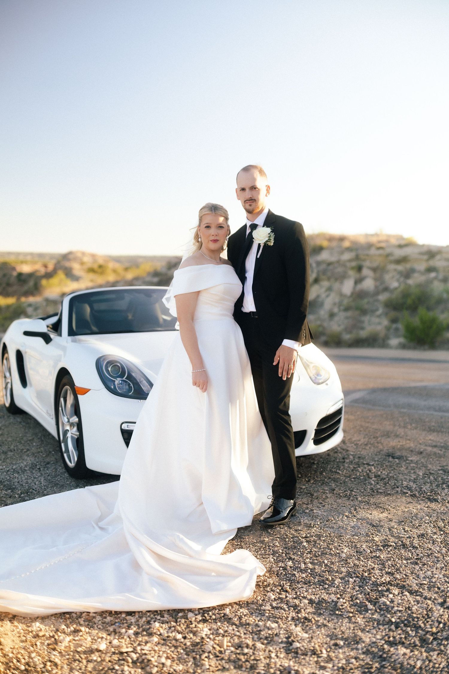 Elegant wedding photos featuring a couple posing with a white luxury sports car in a desert setting.
