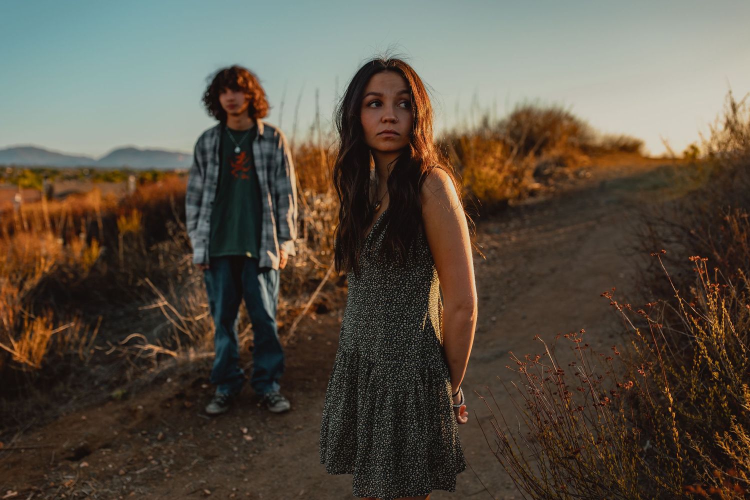Two people stand on a hiking trail at sunset with golden light illuminating the scene.