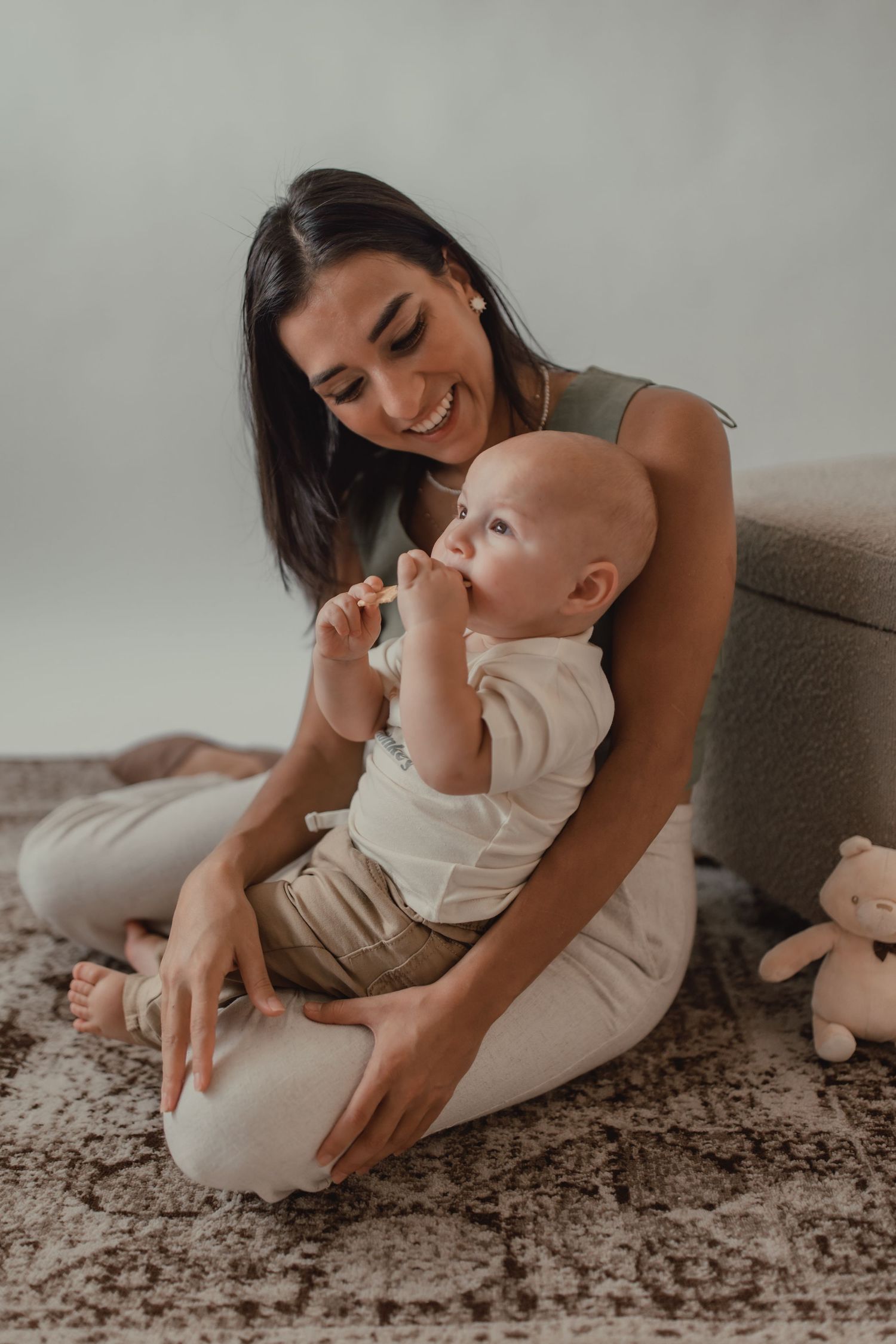 A tender moment between parent and baby sitting on a carpeted floor with a stuffed animal nearby.