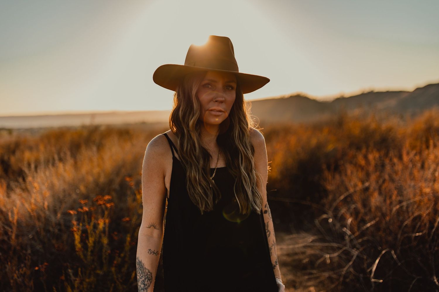 Silhouette portrait with a wide-brimmed hat against a sunset mountain landscape.