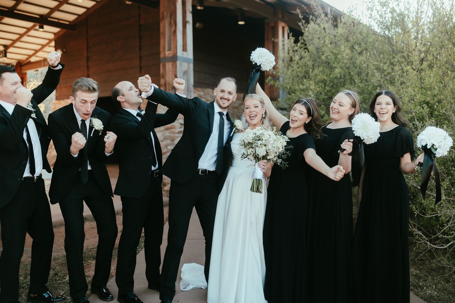 Wedding party members lined up in formal black and white attire at outdoor venue.