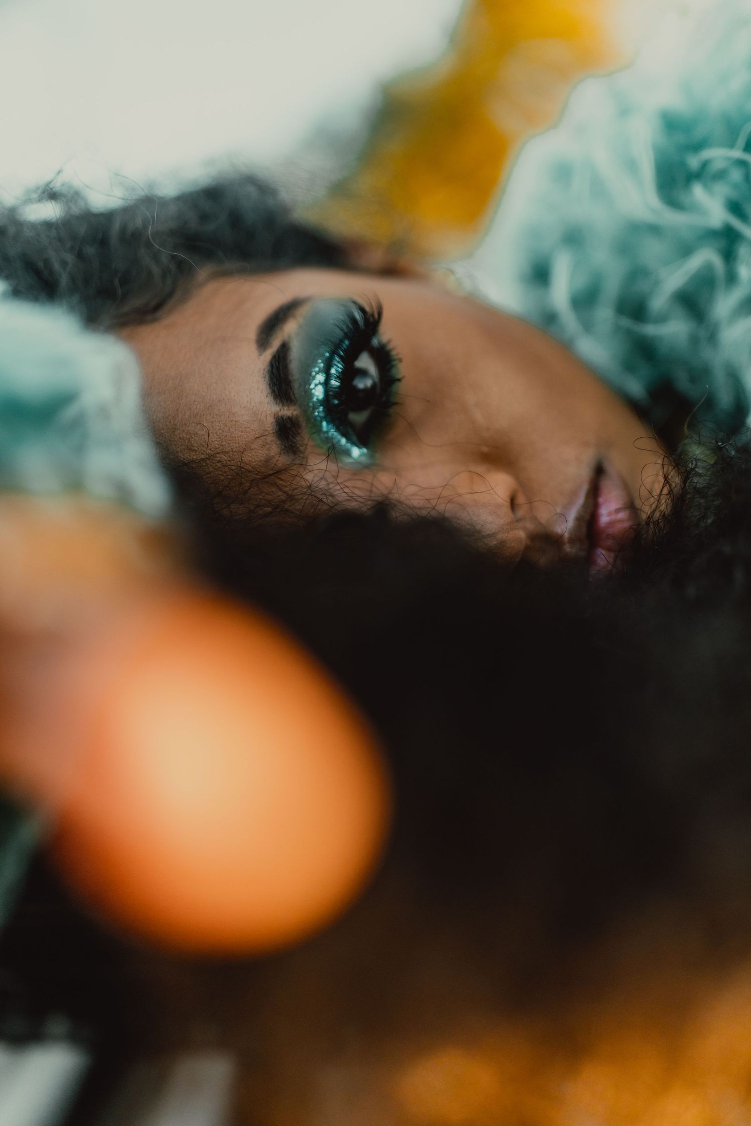 Artistic macro portrait with turquoise eye makeup and orange bokeh lighting effects.