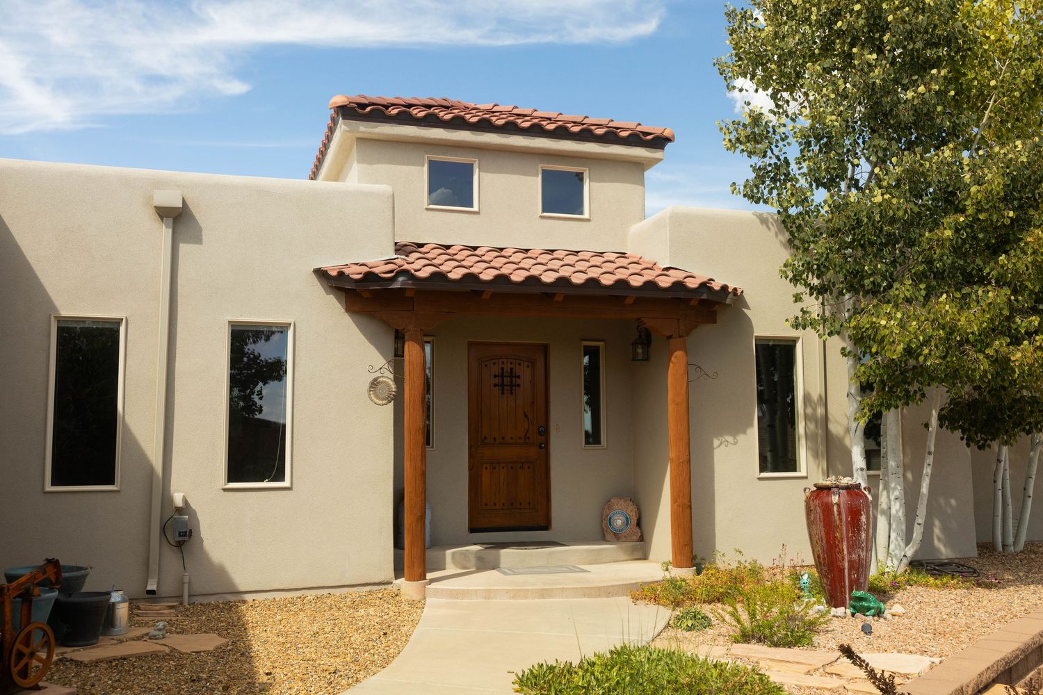 Modern desert home with stucco exterior, wooden posts, and clay tile roof against a bright blue sky.