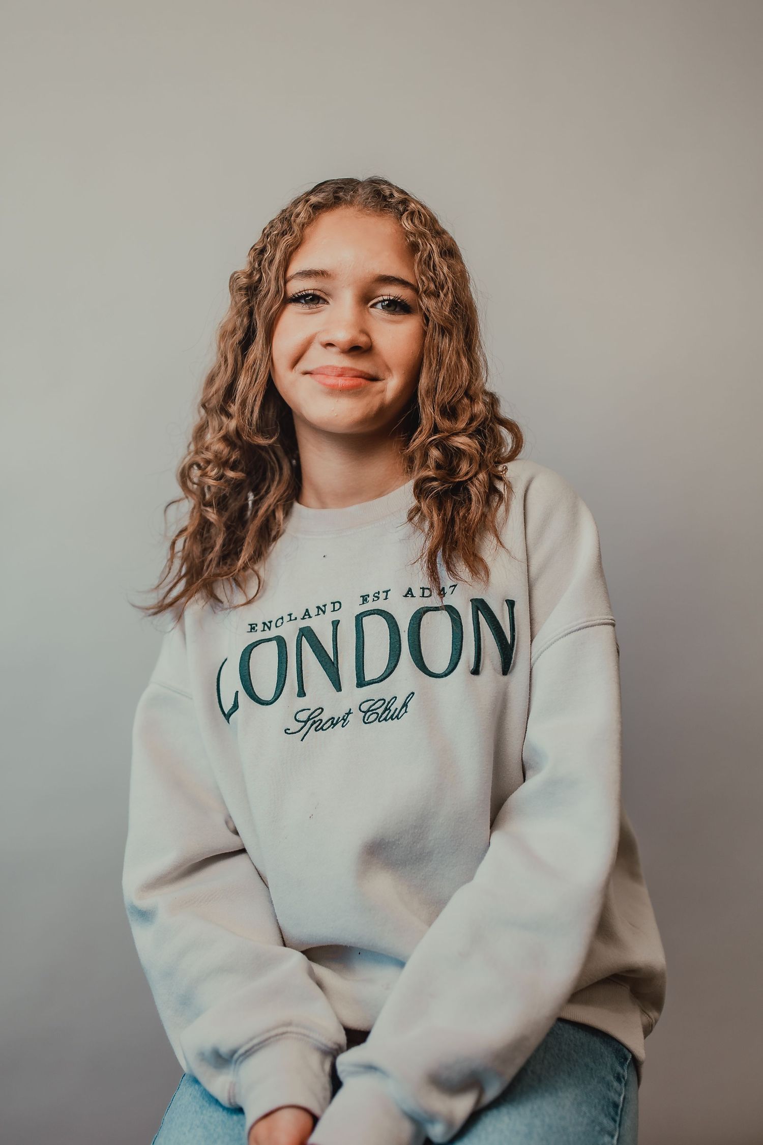 Portrait of someone in a London sweatshirt with curly hair against a gray background.