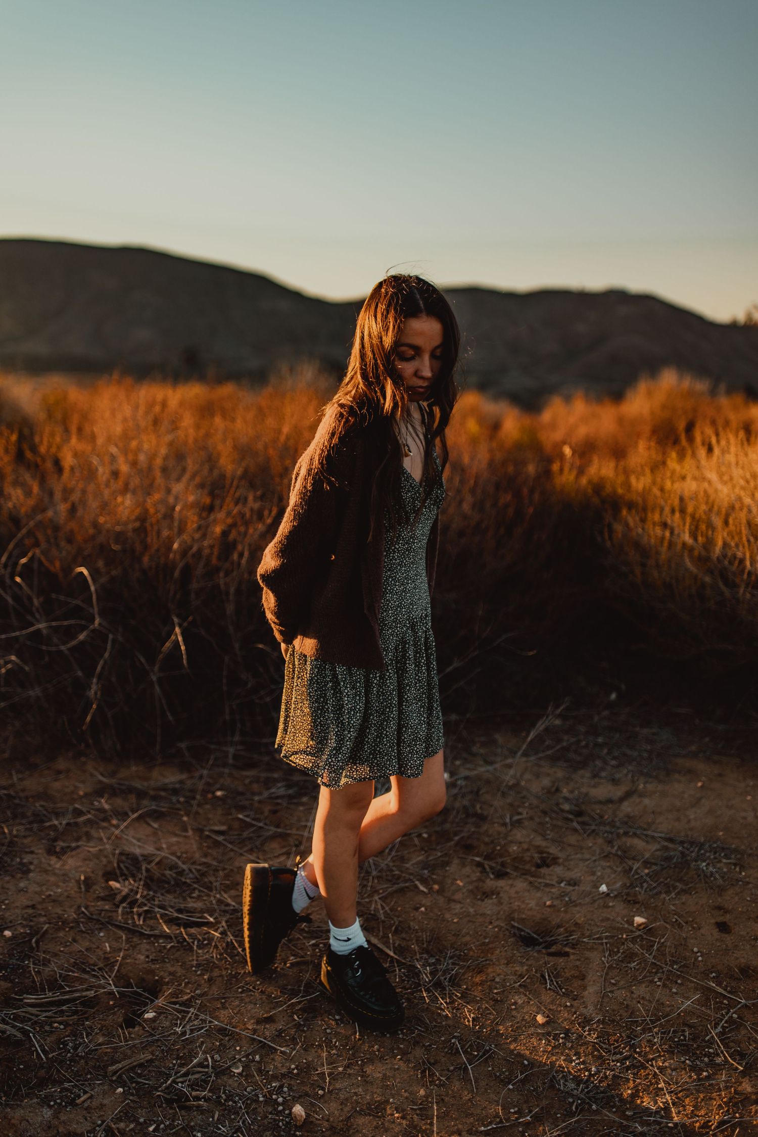 Person in a dress walking through desert brush during golden hour sunset.