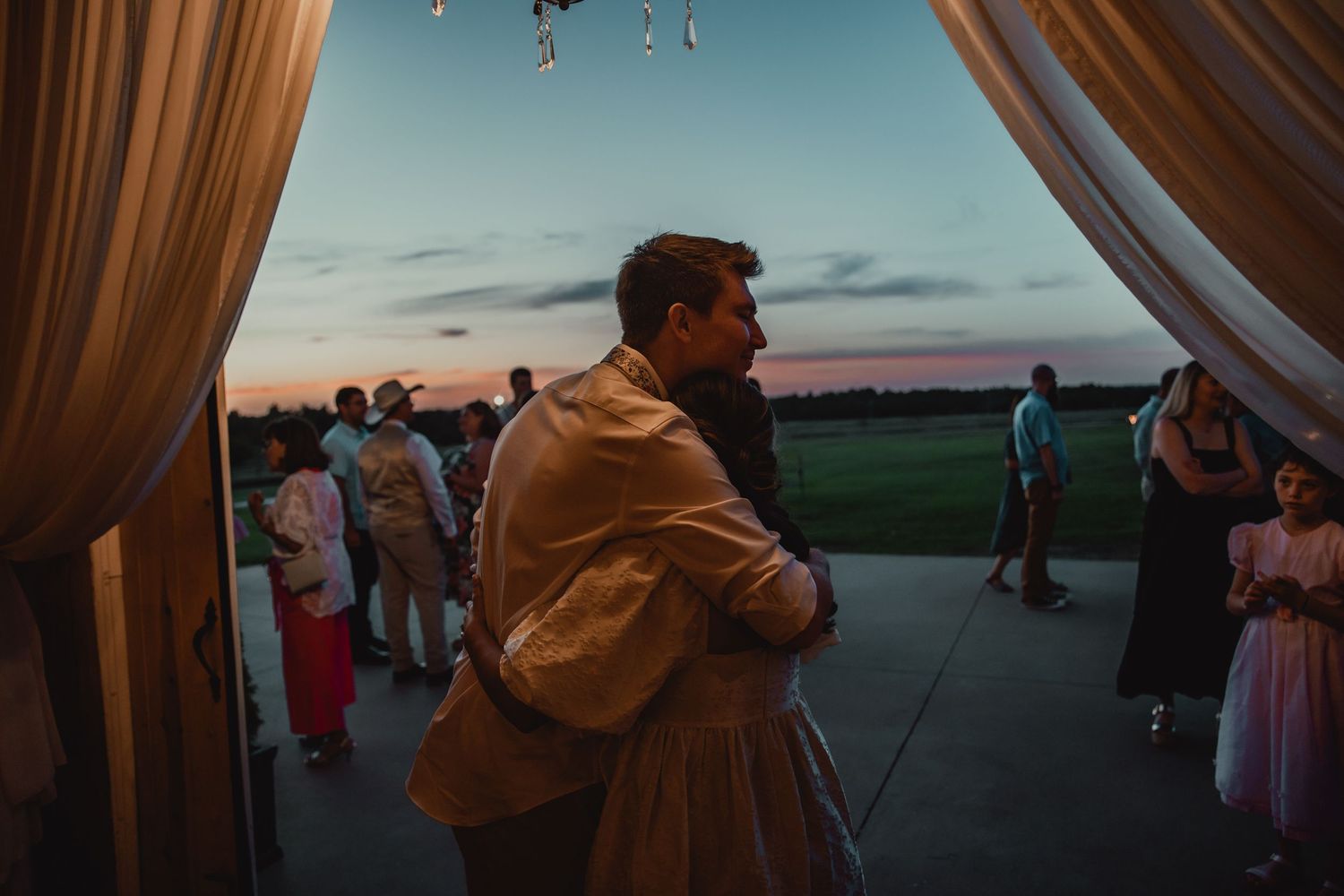Outdoor celebration at dusk with hanging lights and guests mingling on a patio.
