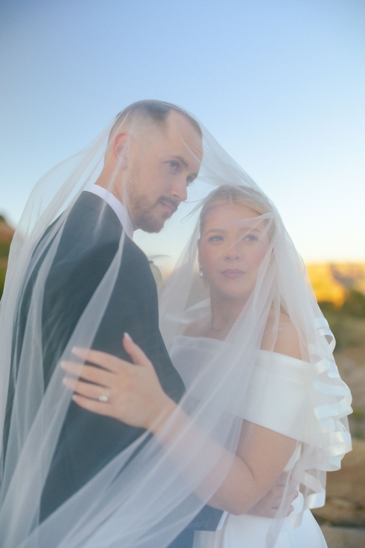 Intimate wedding moment captured through sheer veil during golden hour.