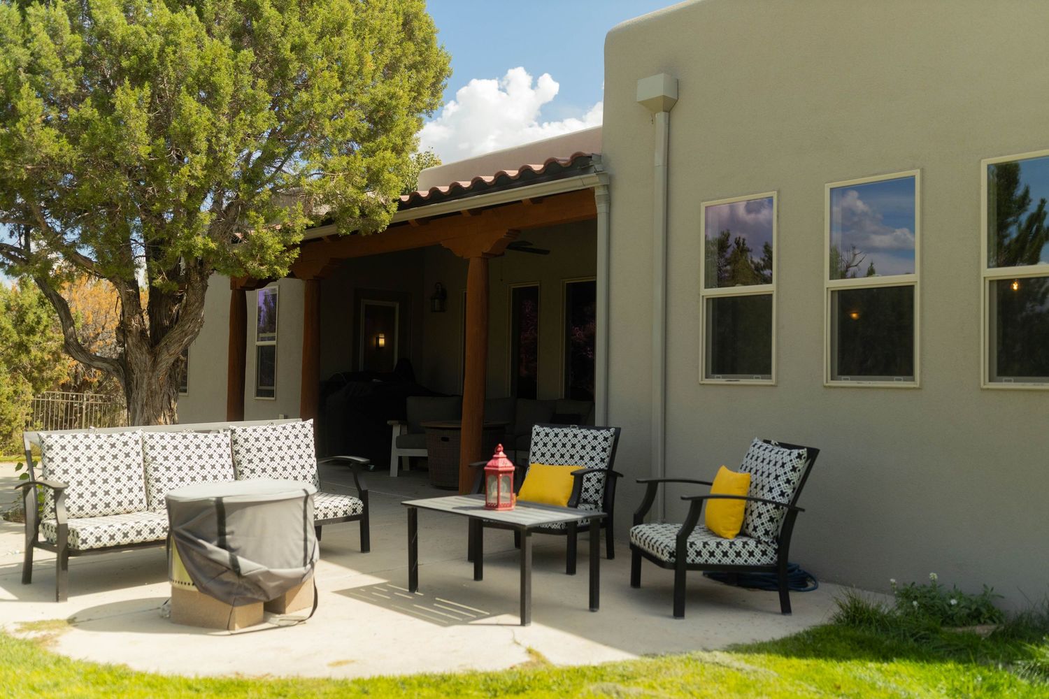 Modern patio seating area with black and white cushioned chairs and yellow accent pillows under a covered pergola.