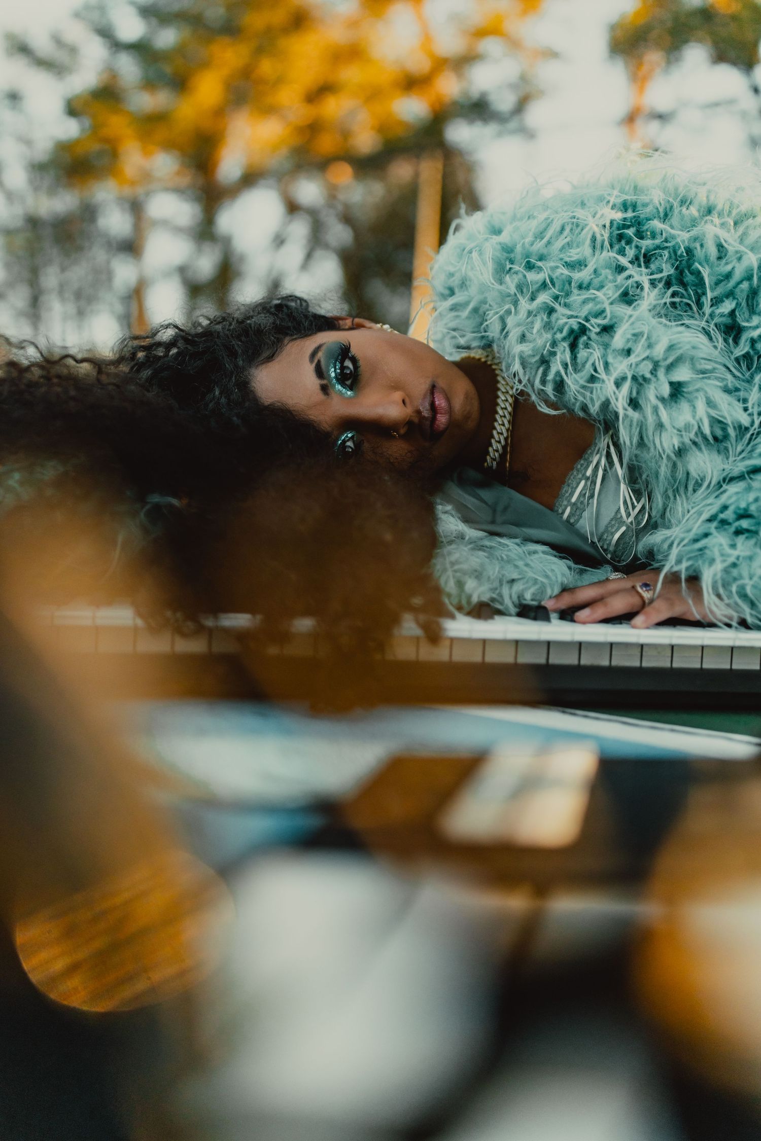 Artistic portrait with teal feathers and piano keys in soft natural lighting.