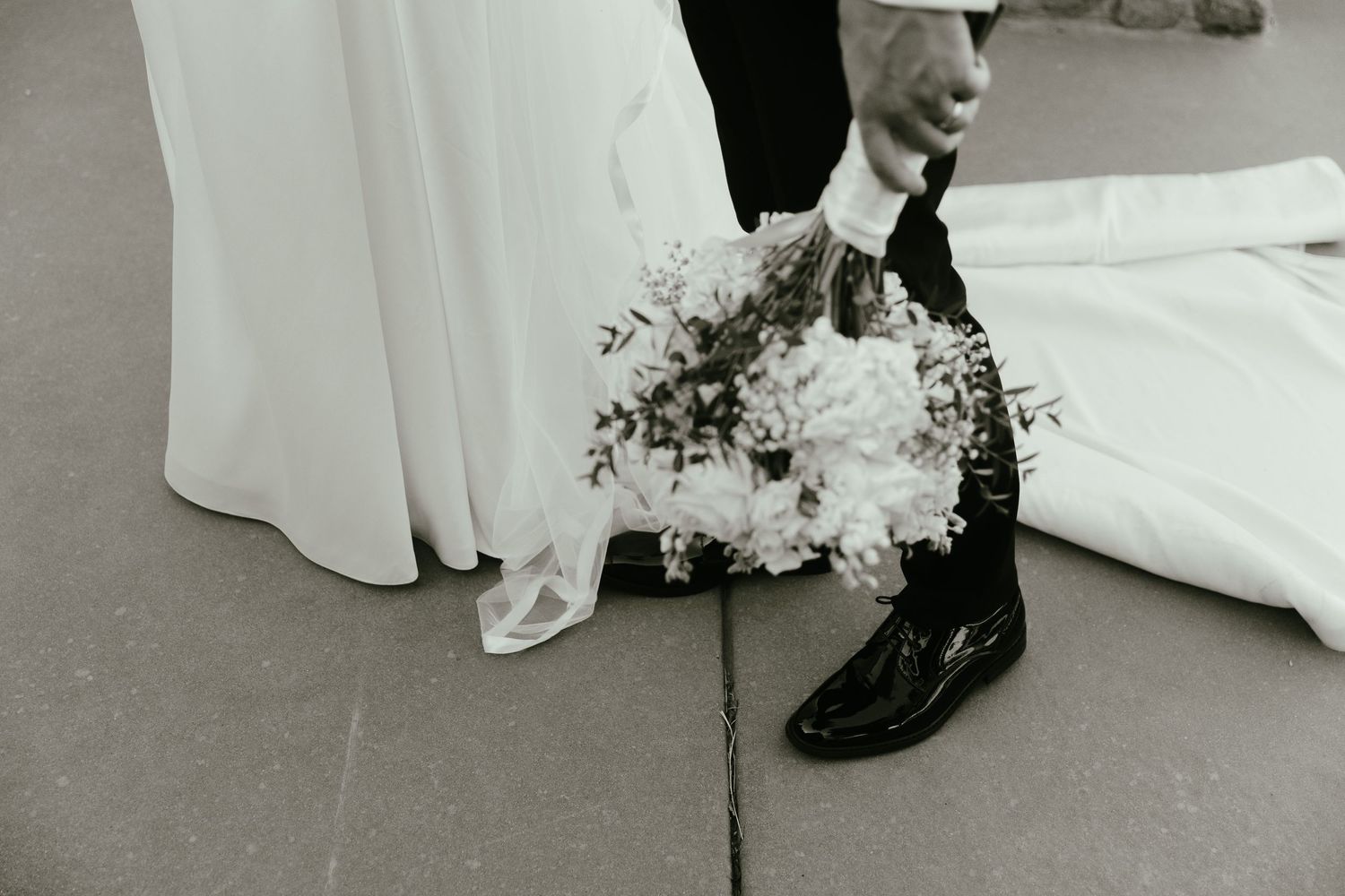 Close-up details of wedding shoes and dress hem on stone pathway.