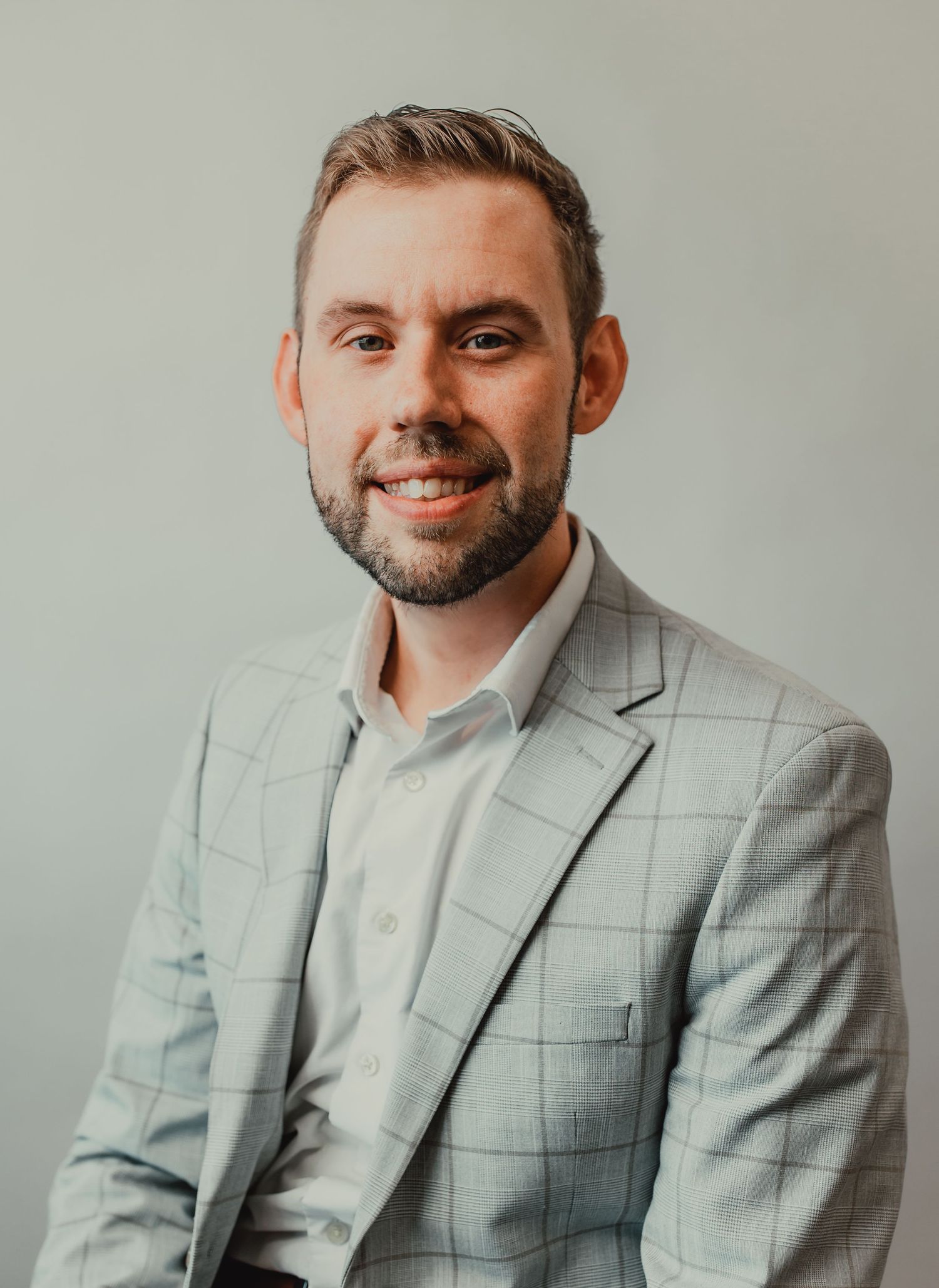 Professional headshots of person in light gray checkered suit against neutral background.