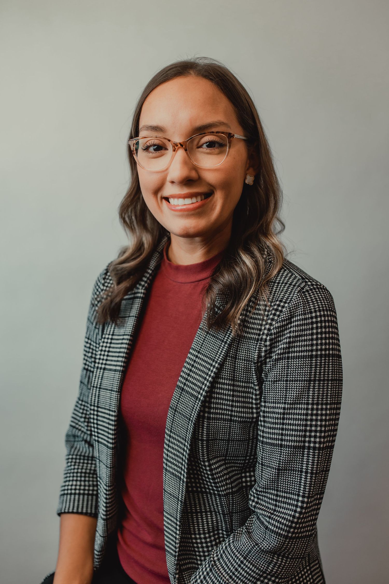 Professional portraits in plaid blazer and burgundy top against gray backdrop.