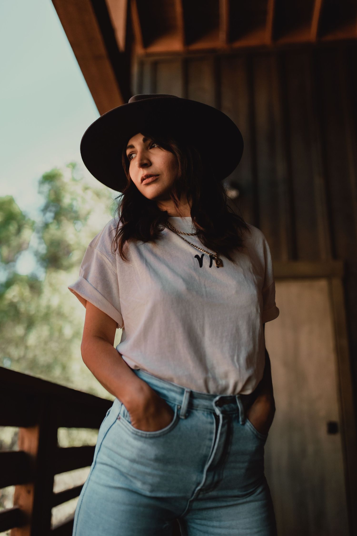 Casual portrait of someone in jeans and hat standing on a wooden porch.