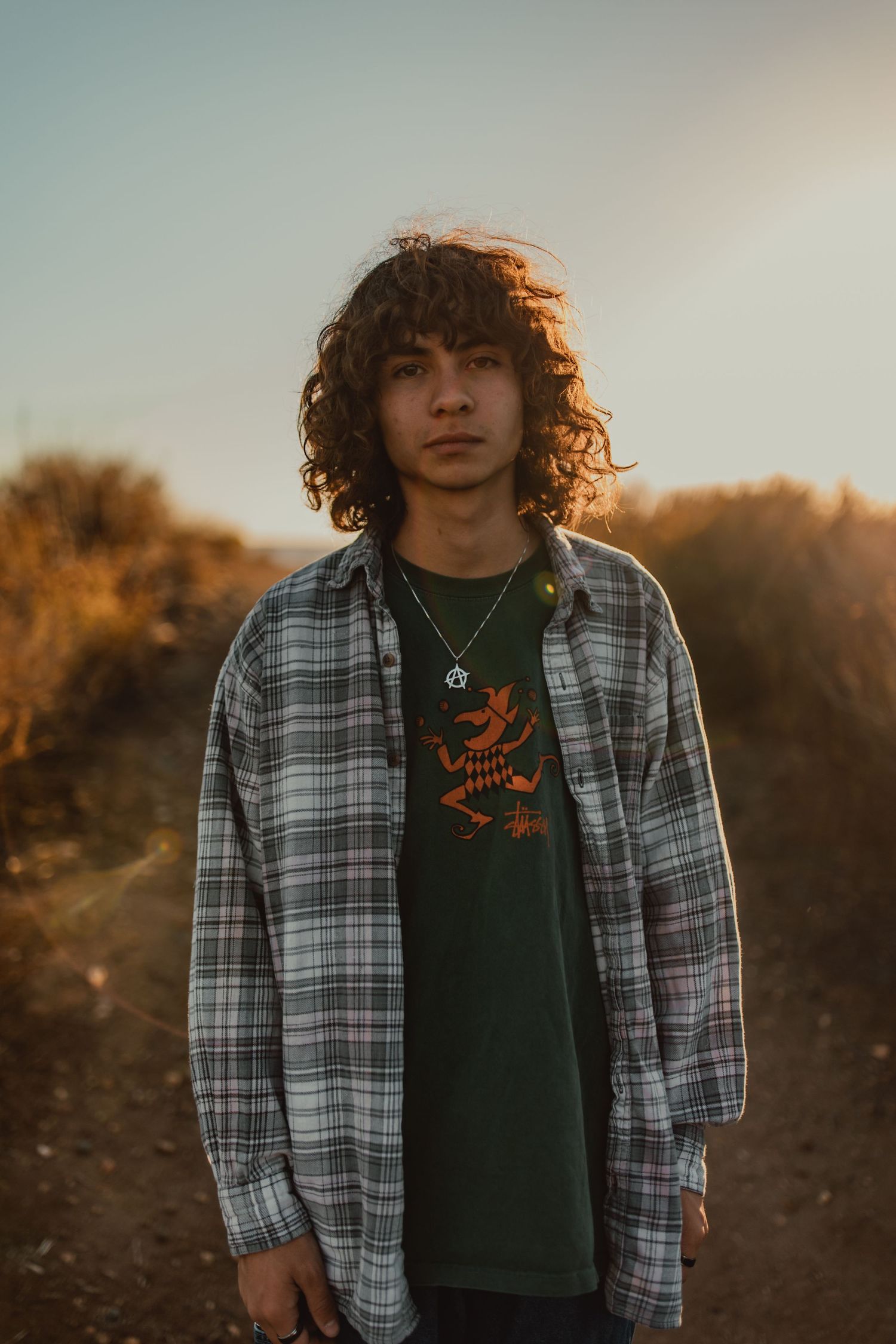 Portrait of someone in plaid shirt and graphic tee standing in golden hour light.