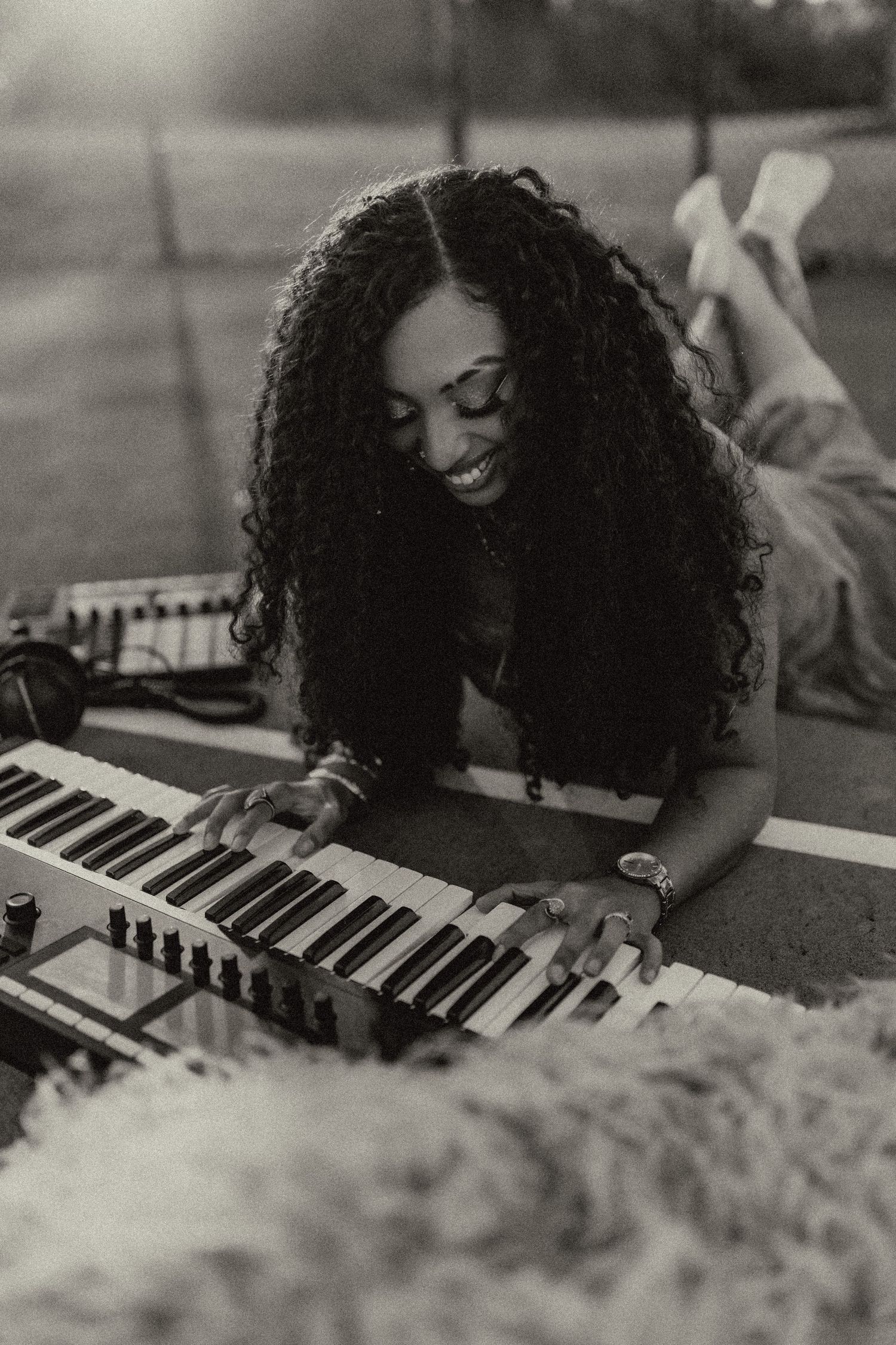 A black and white photo of a musician playing keyboard while lying on a blanket.