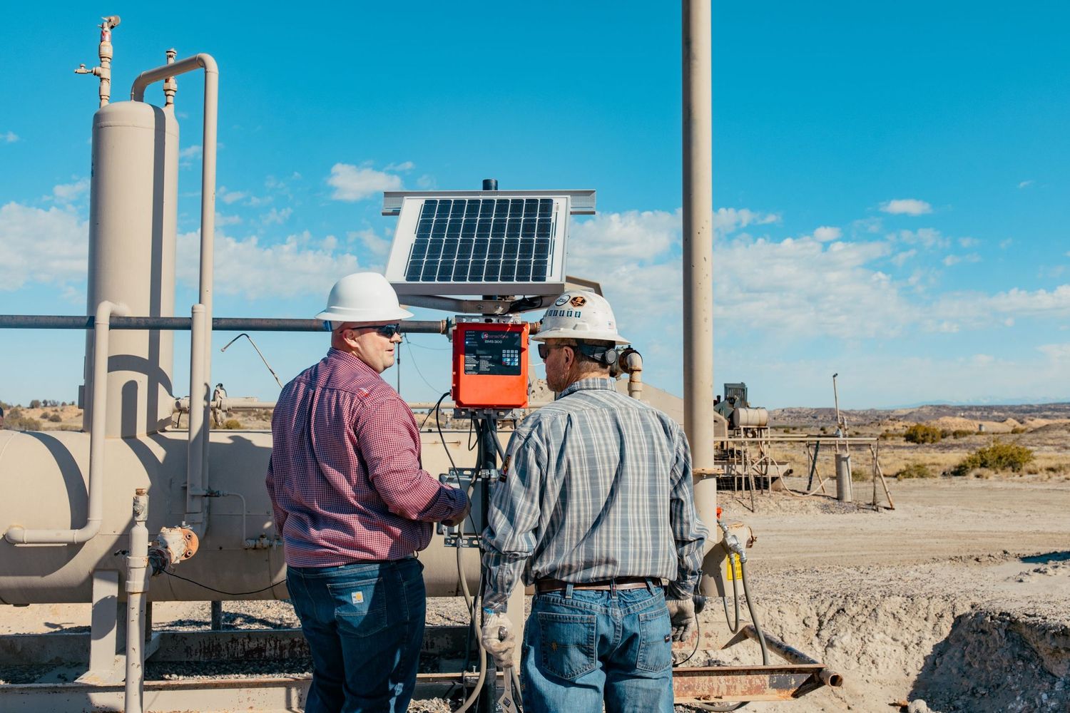 Two workers examining solar panel equipment in an industrial outdoor setting.