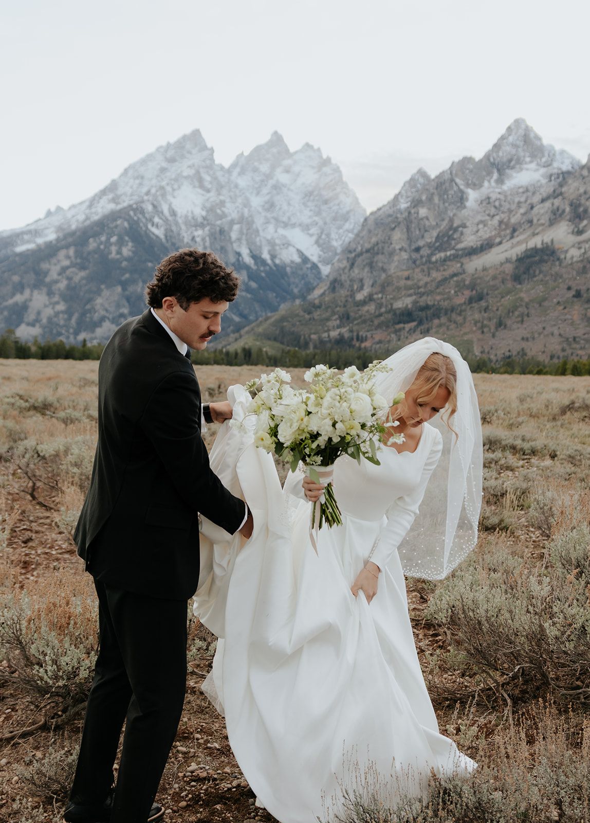 Groom carrying bride's wedding dress train in Grand Teton National Park during bridal photoshoot