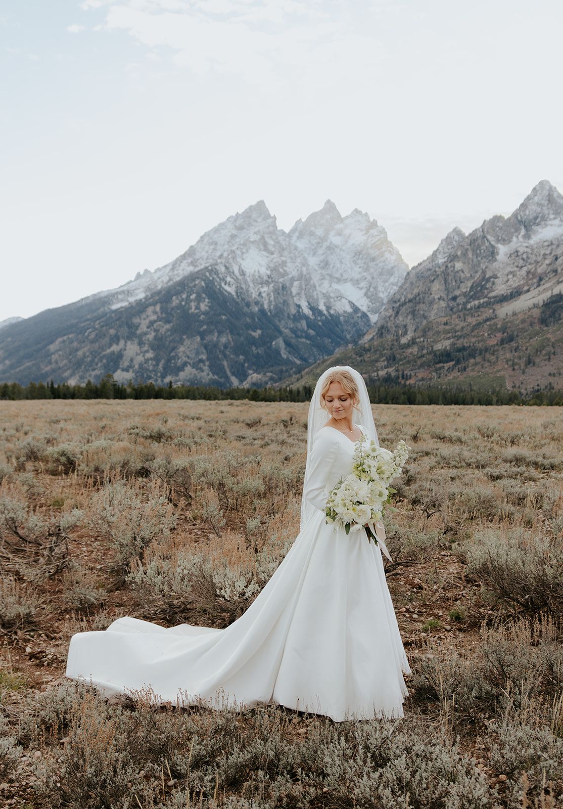Bridal photoshoot in Grand Teton National Park. Long sleeve wedding dress, long wedding dress train, long veil with pearls. Margene's Bridal
