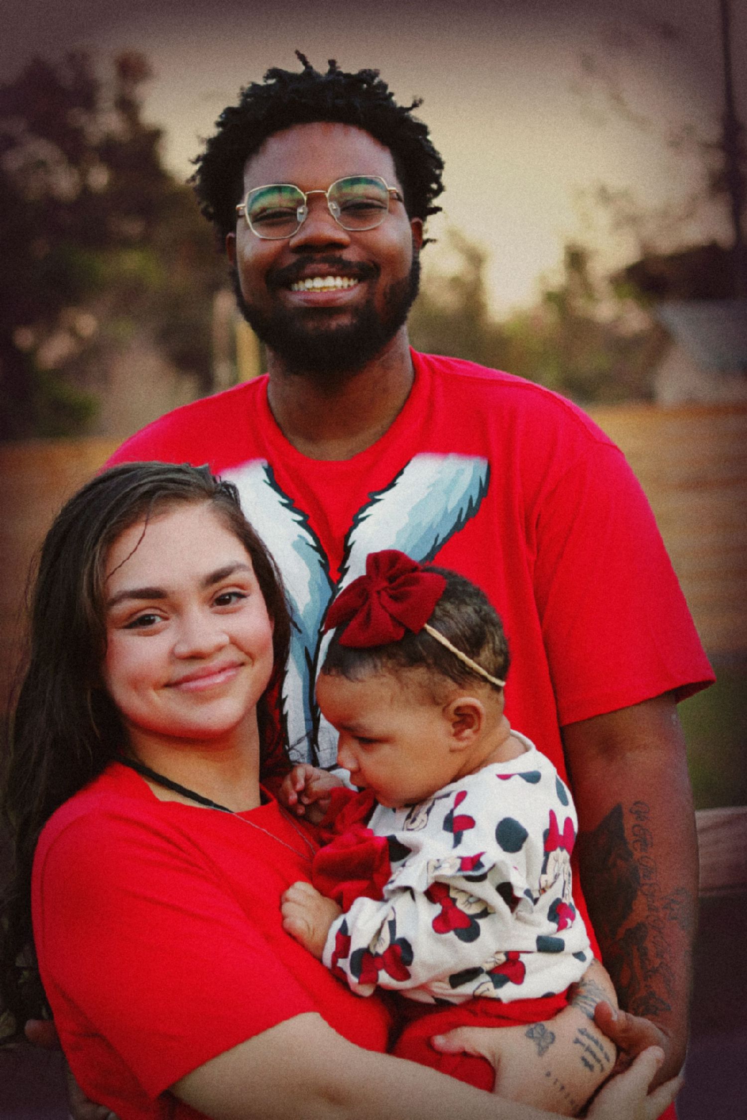 Family in matching red outfits poses together during outdoor photo session.