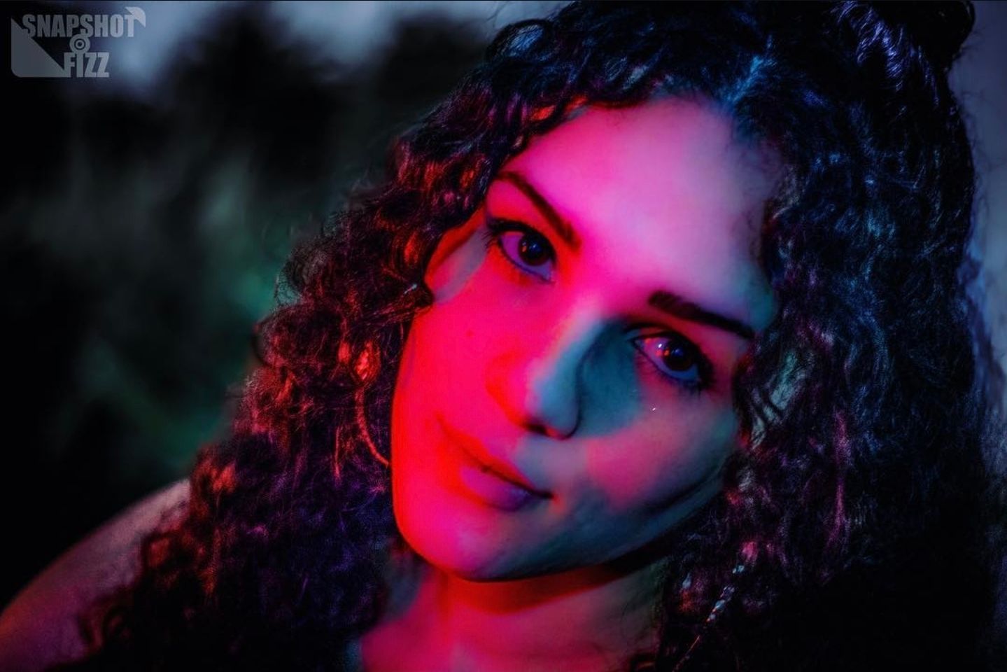 Artistic portrait with dramatic pink and blue lighting effects.