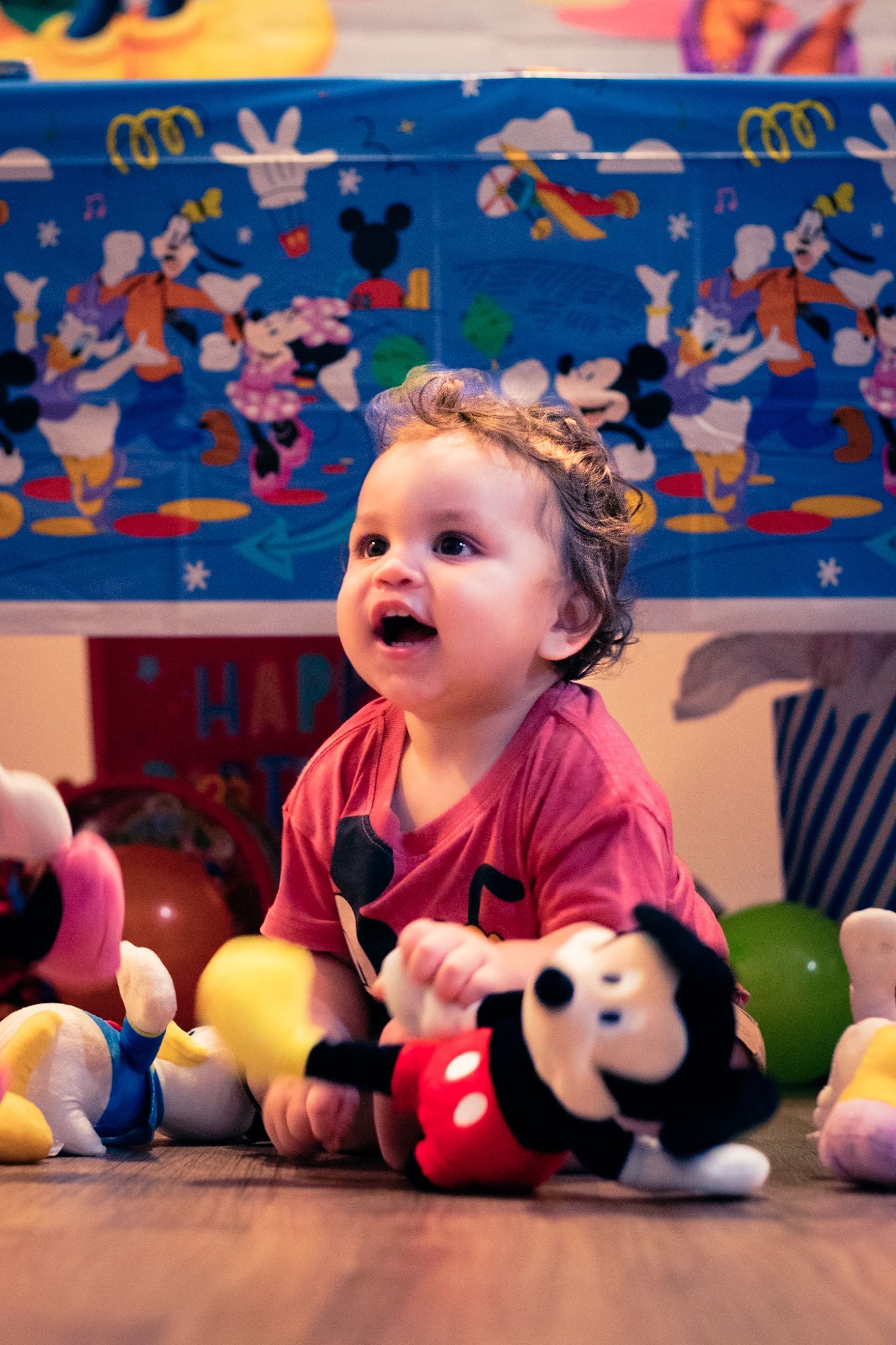 A child plays on floor with Disney plush toys and colorful decorations in background.