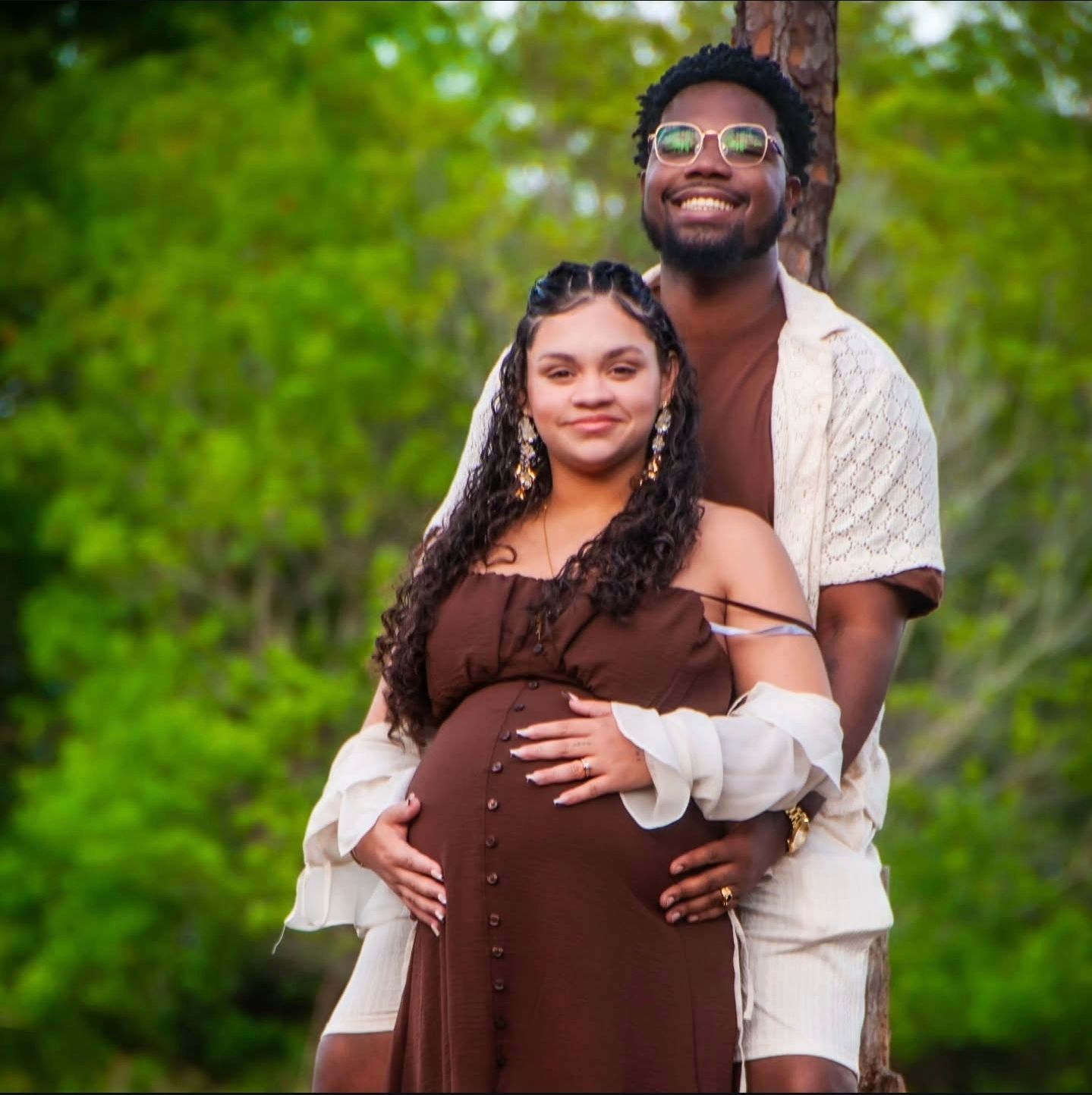 Expectant couple embracing outdoors in a garden setting with natural greenery.
