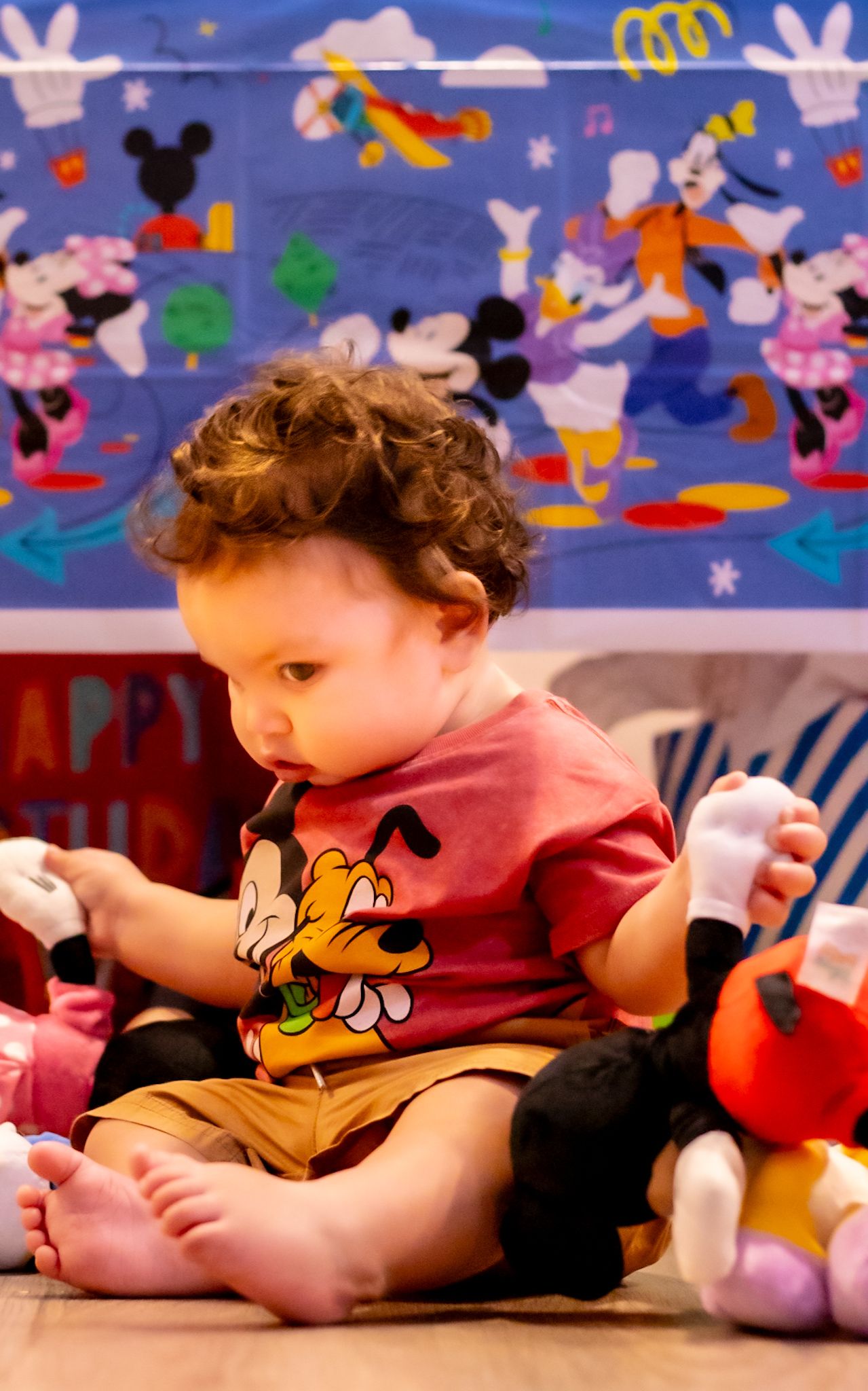 Baby lying on floor wearing Mickey Mouse outfit with Disney character decorations on wall.