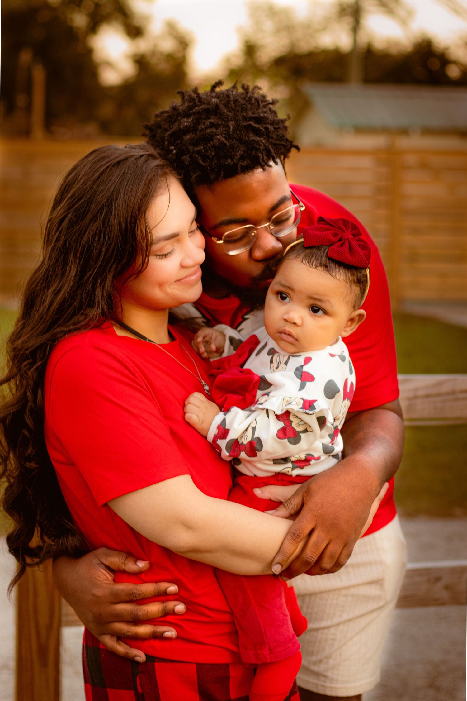 Family shares warm embraces while wearing coordinated red outfits during sunset photoshoot.