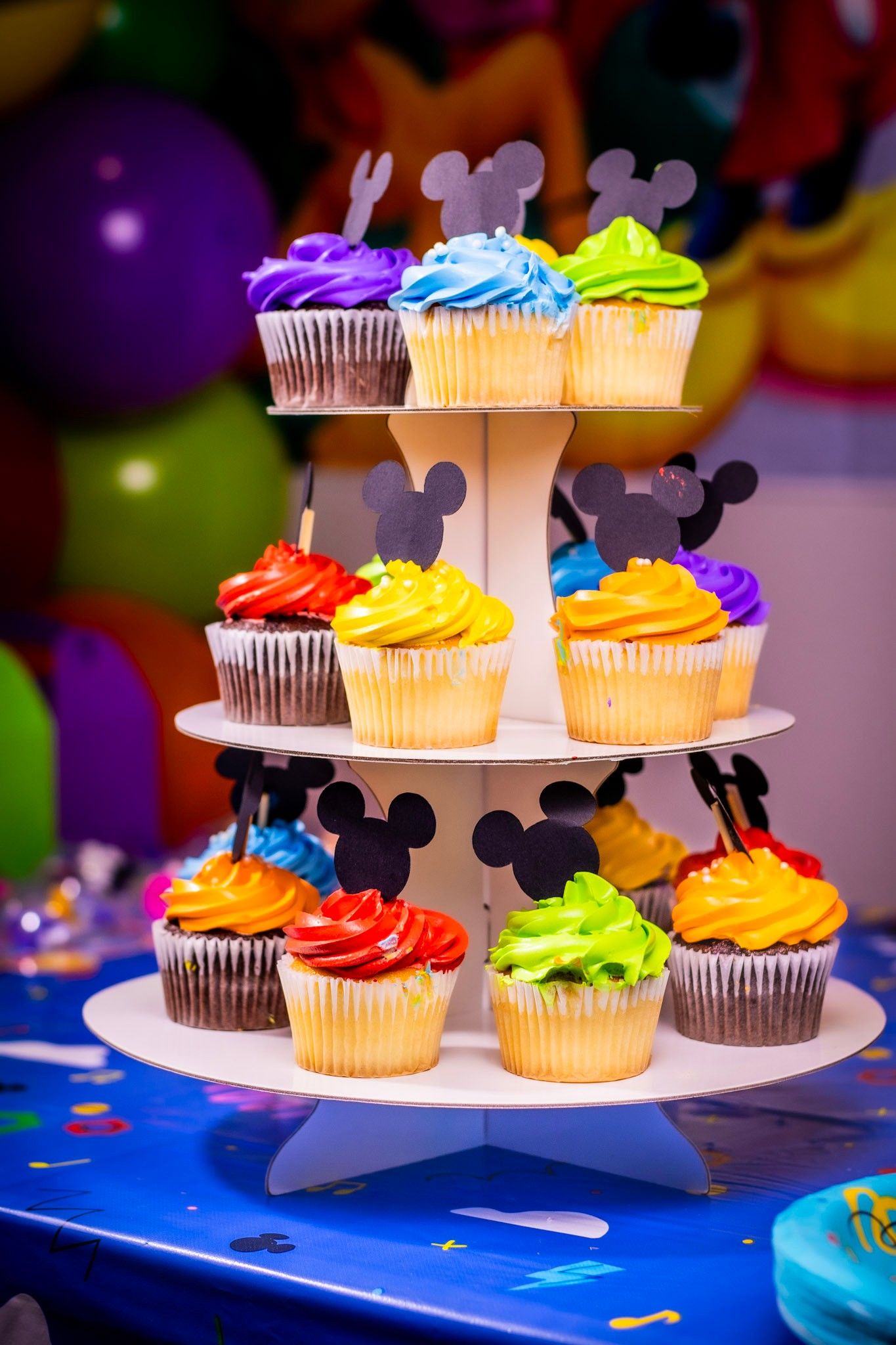 Colorful cupcakes with Mickey Mouse decorations displayed on a tiered white stand.