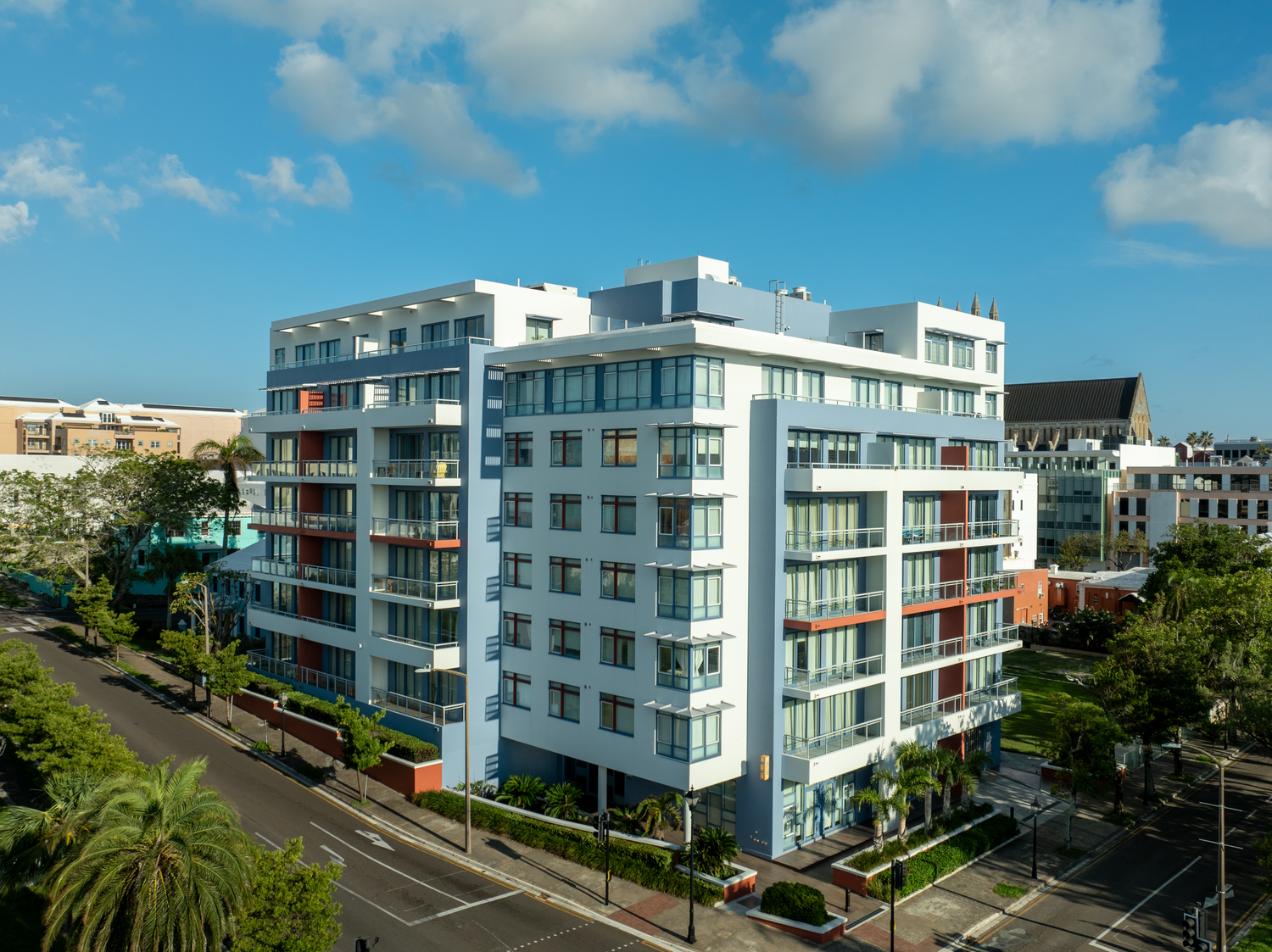 Modern white apartment buildings with balconies line a coastal street under blue skies. Drone photogrpahy.