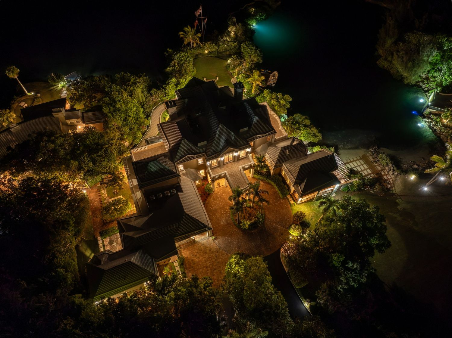 Bird's eye perspective of an upscale property with strategic landscape lighting at night. Drone photogrpahy.