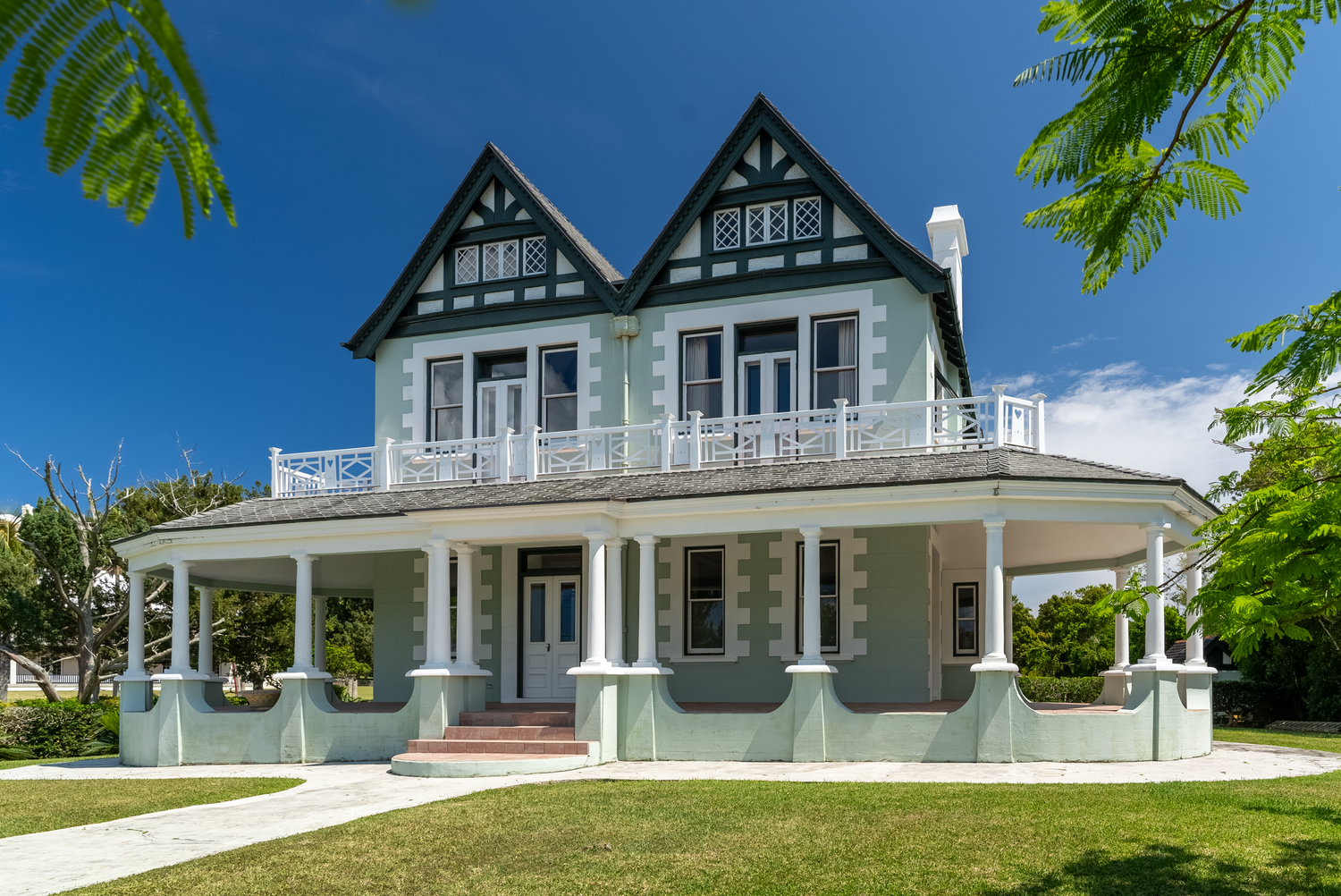 Panoramic view of luxury waterfront homes with white trim and green shutters against blue sky and palm trees.