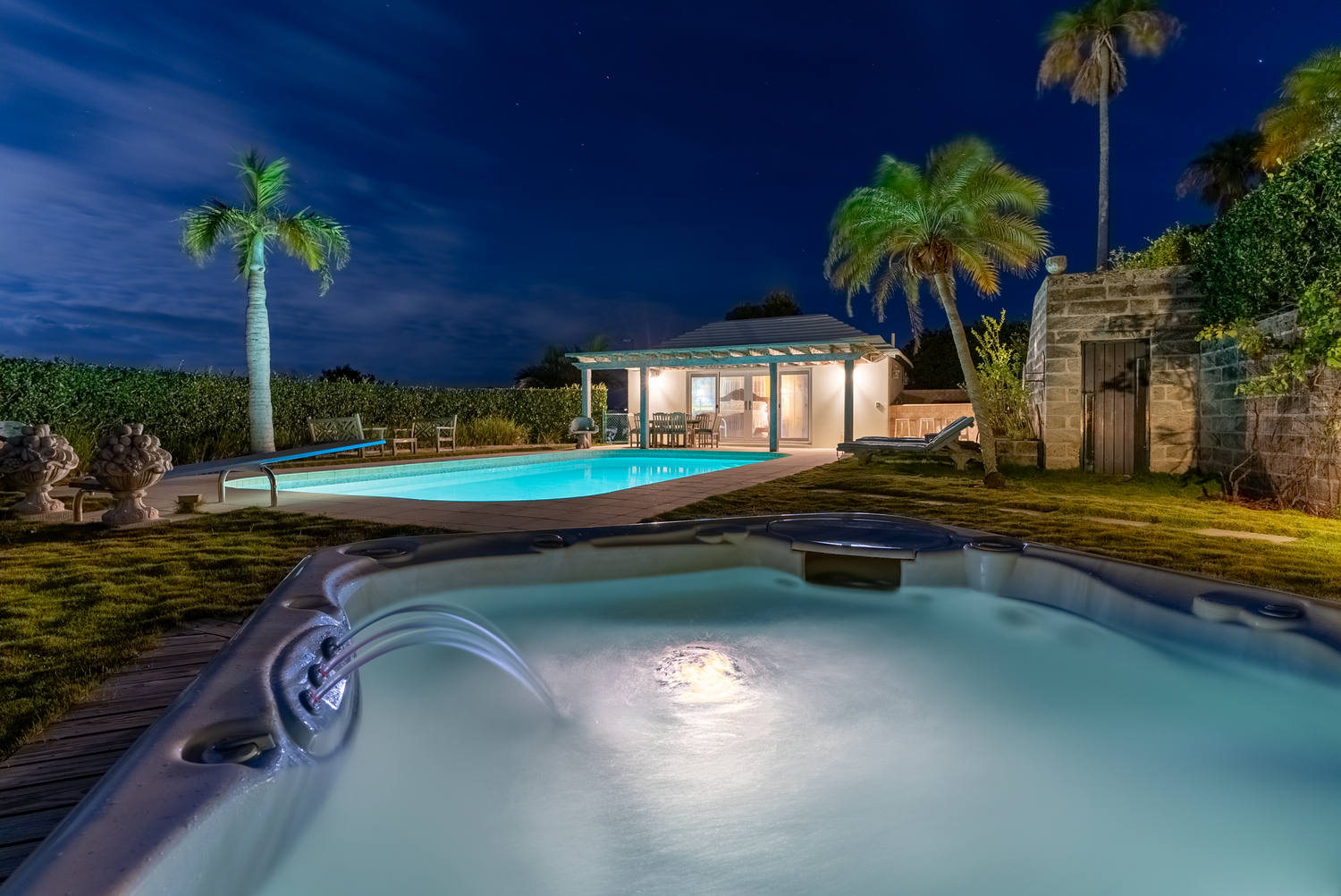 Illuminated swimming pool at night surrounded by palm trees and tropical landscaping.