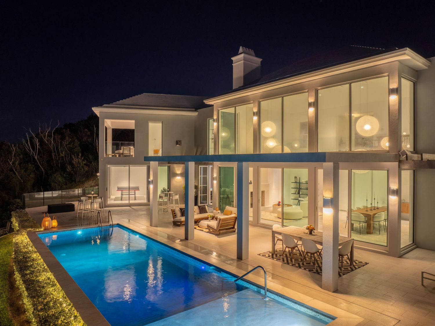 Contemporary white house with illuminated swimming pool and outdoor living spaces at dusk. Drone photogrpahy.