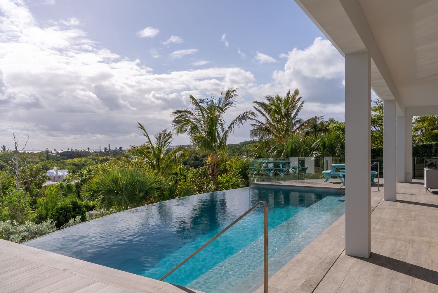 Luxurious infinity pool overlooking tropical landscape with white columns and lounge chairs.