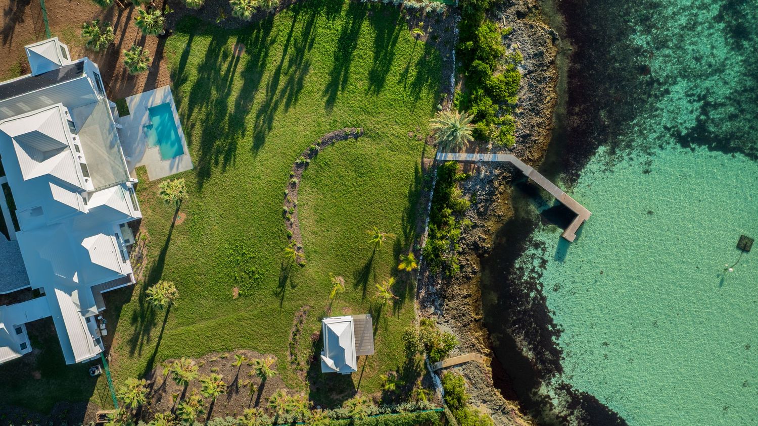 Aerial panorama of coastal properties with swimming pools and tropical gardens along turquoise waters. Drone photogrpahy.