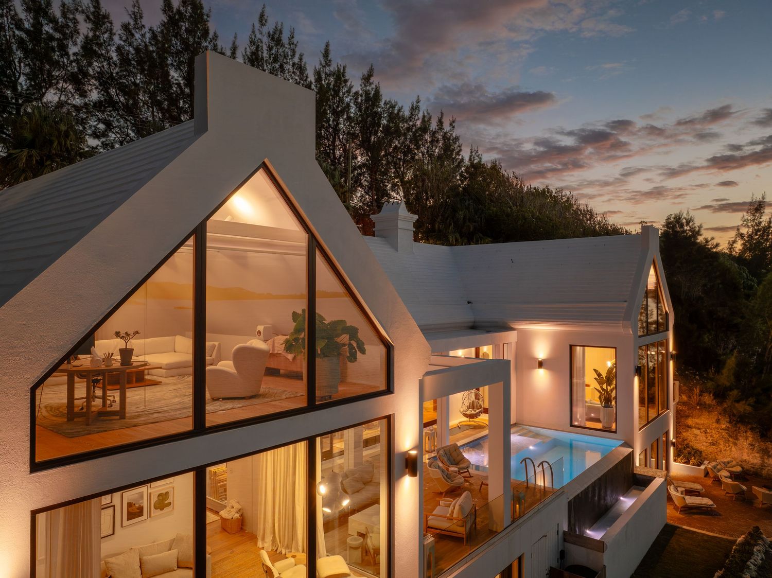 Modern A-frame cottages illuminated at sunset with warm glowing windows and dramatic sky. Drone photogrpahy.
